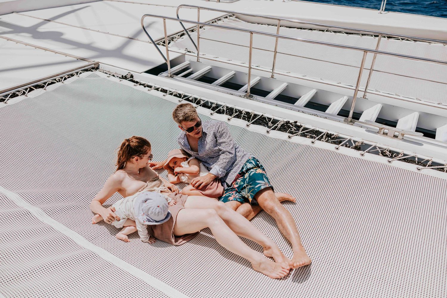 Couple relaxing on catamaran deck net with drinks enjoying a sunny day at sea.