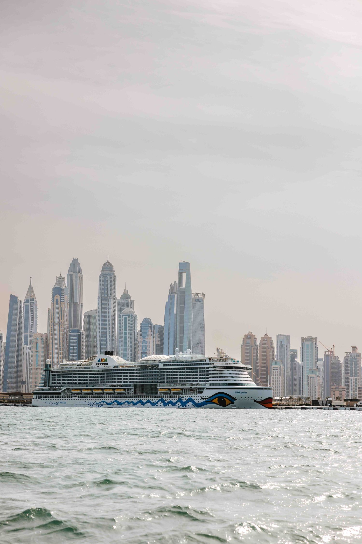 Large AIDA cruise ship docked near Dubai Marina with towering skyscrapers in the background.