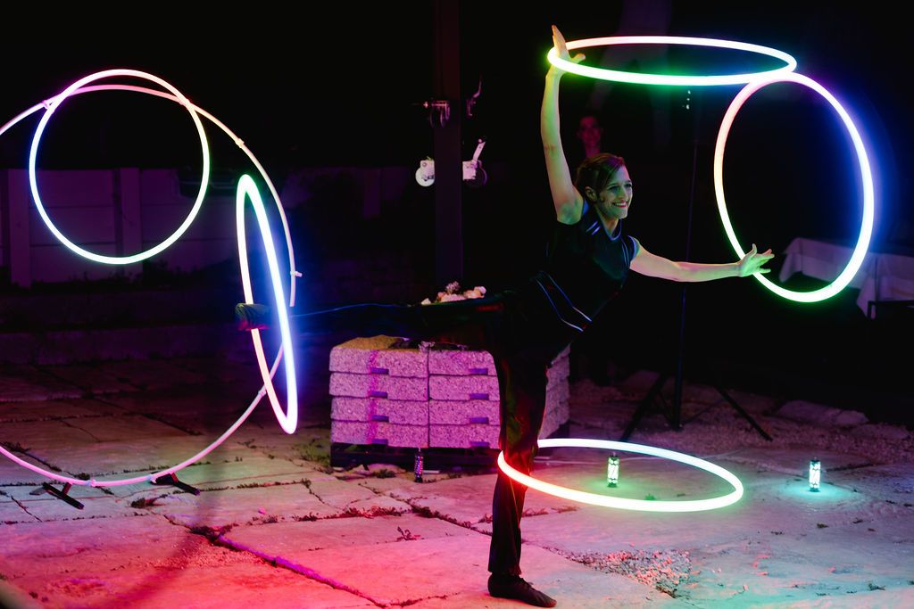 Acrobatic performer spinning multiple glowing neon hula hoops in colorful light display at night show.