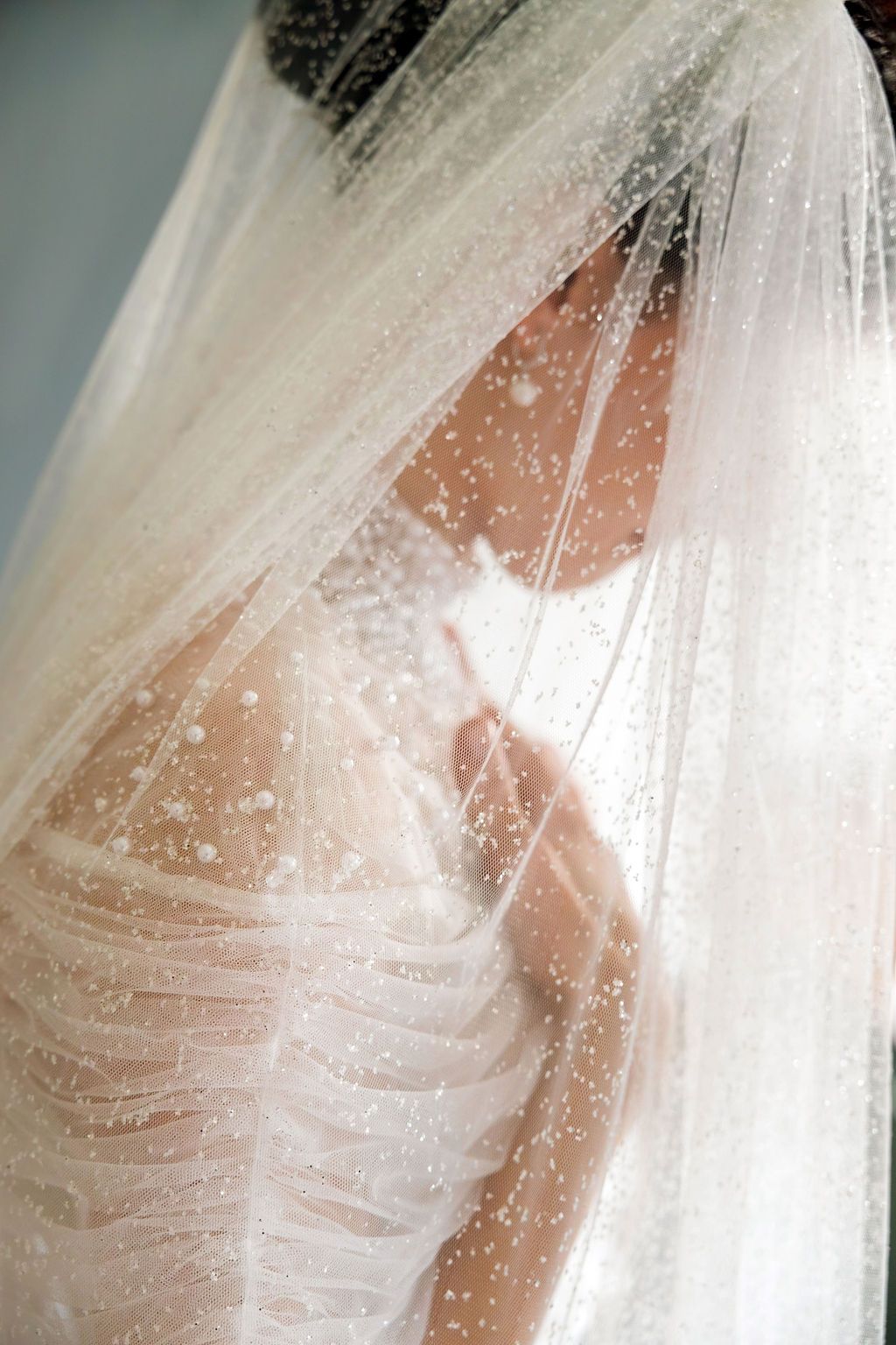 Close-up of bride wearing sparkling embellished wedding veil with delicate pearl details in soft light.