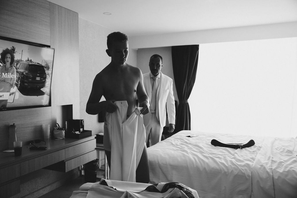 Black and white photo of two men getting ready in a hotel room before a wedding.