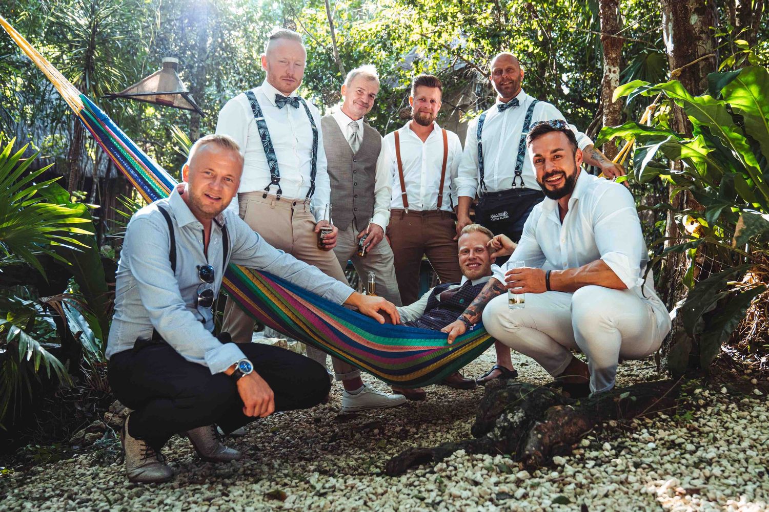 Group of groomsmen posing together in a lush tropical garden with one relaxing in a hammock.