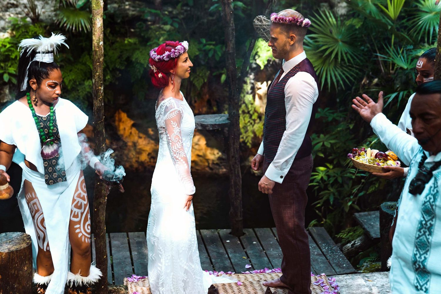 Boho jungle wedding ceremony with bride in lace dress and groom, officiated by tattooed priestess with incense.