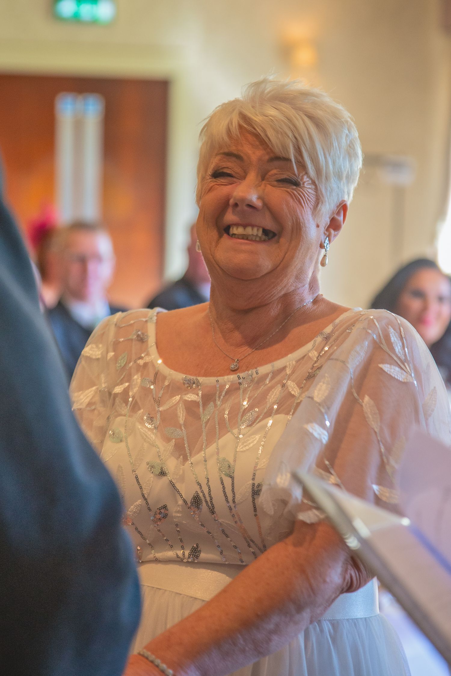 Wedding guest in white lace dress dancing and smiling at indoor reception.