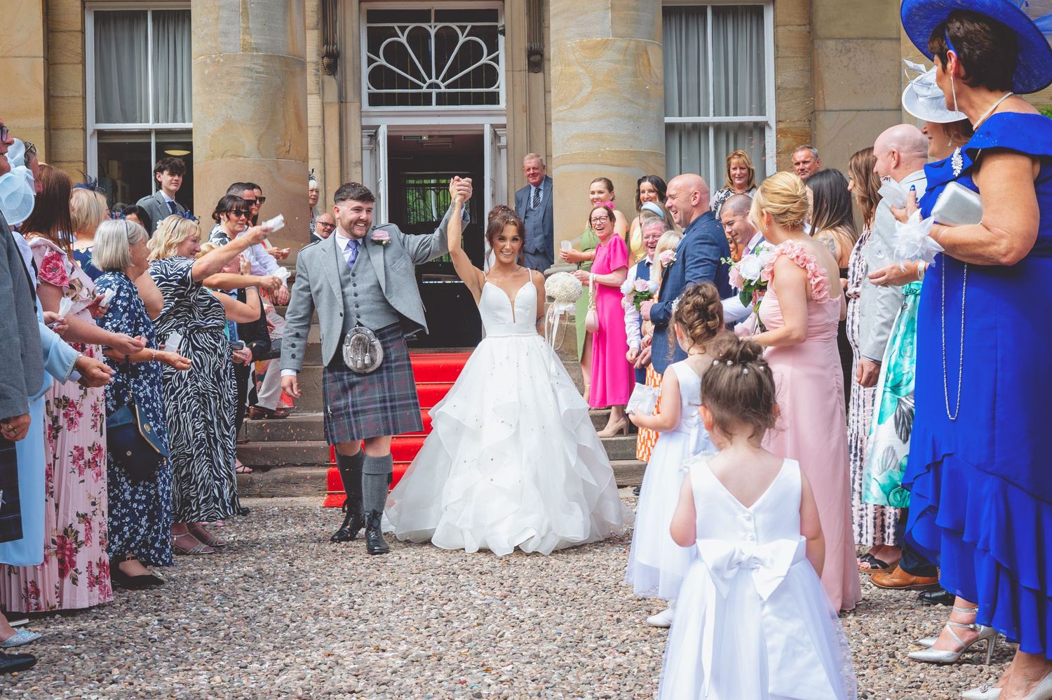Wedding guests line up outside a grand stone building for the celebration.
