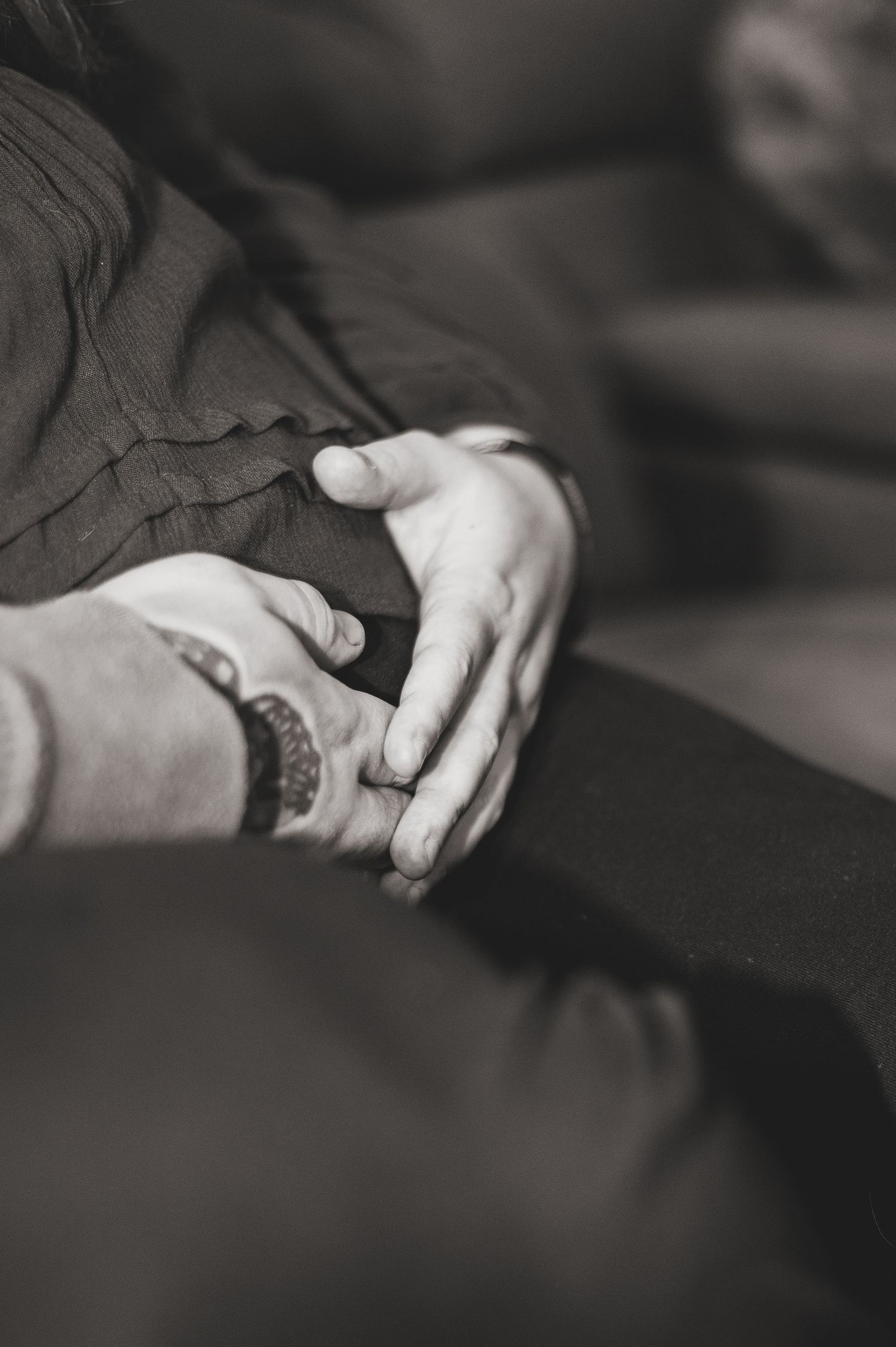 Close-up black and white image showing hands with tattoos in a dramatic lighting setting.