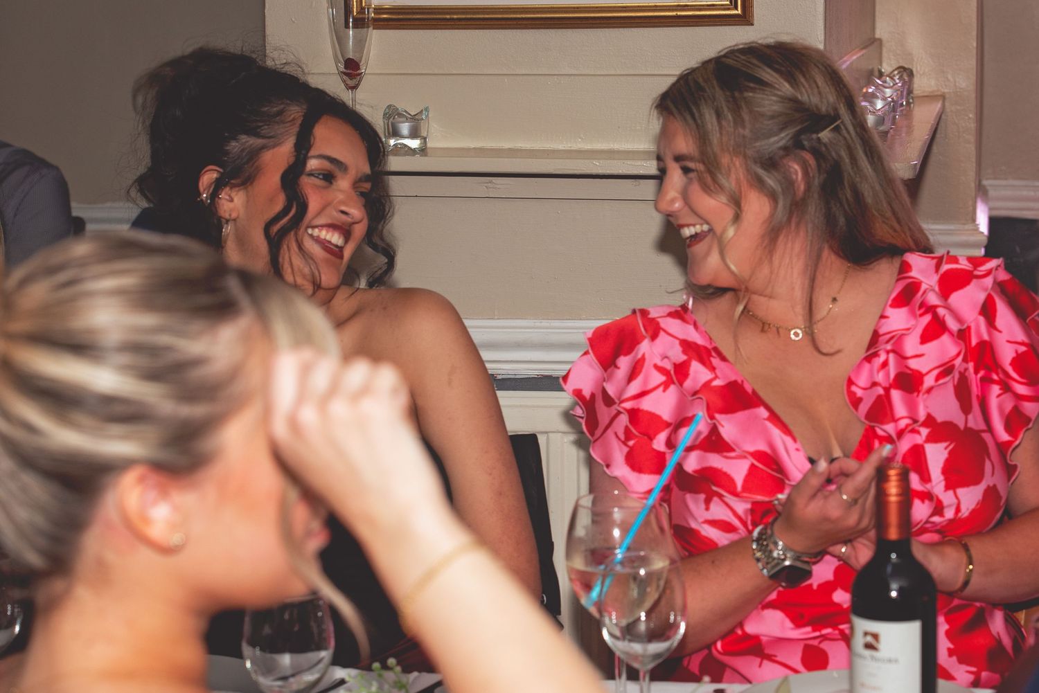 Wedding guests share laughter and conversation over wine at an elegant reception dinner.