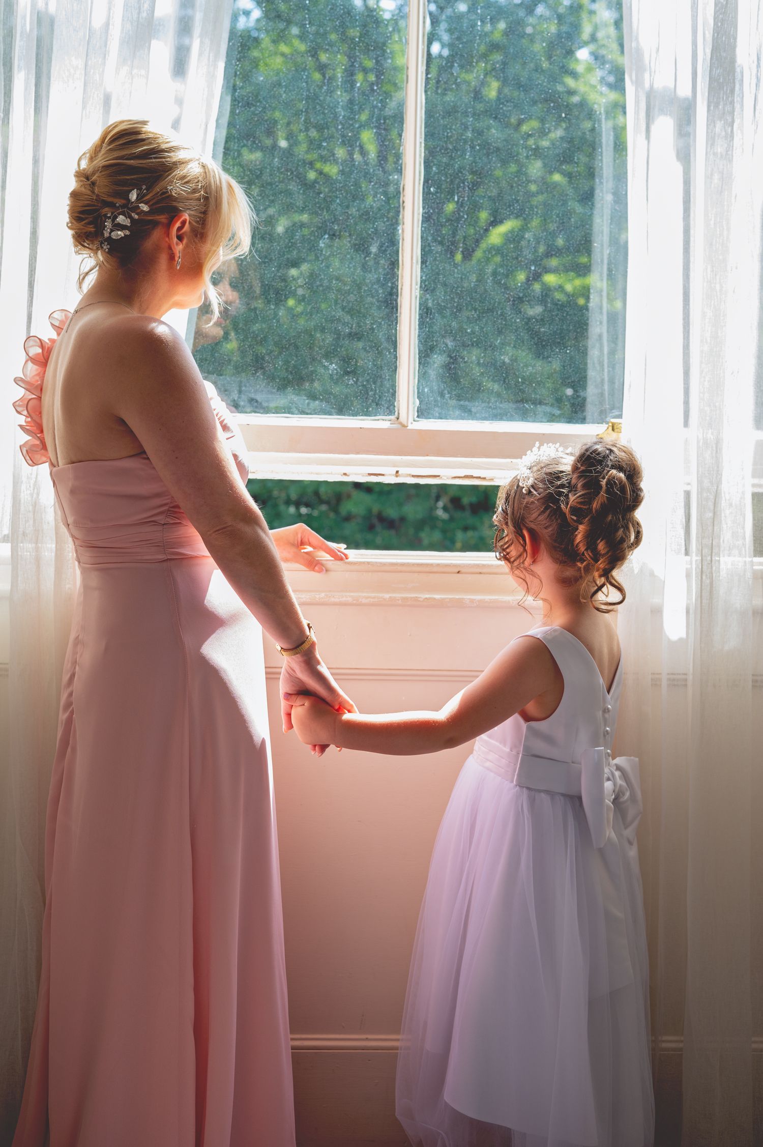 Bridesmaid in pink dress helps adjust a young flower girl's white dress.