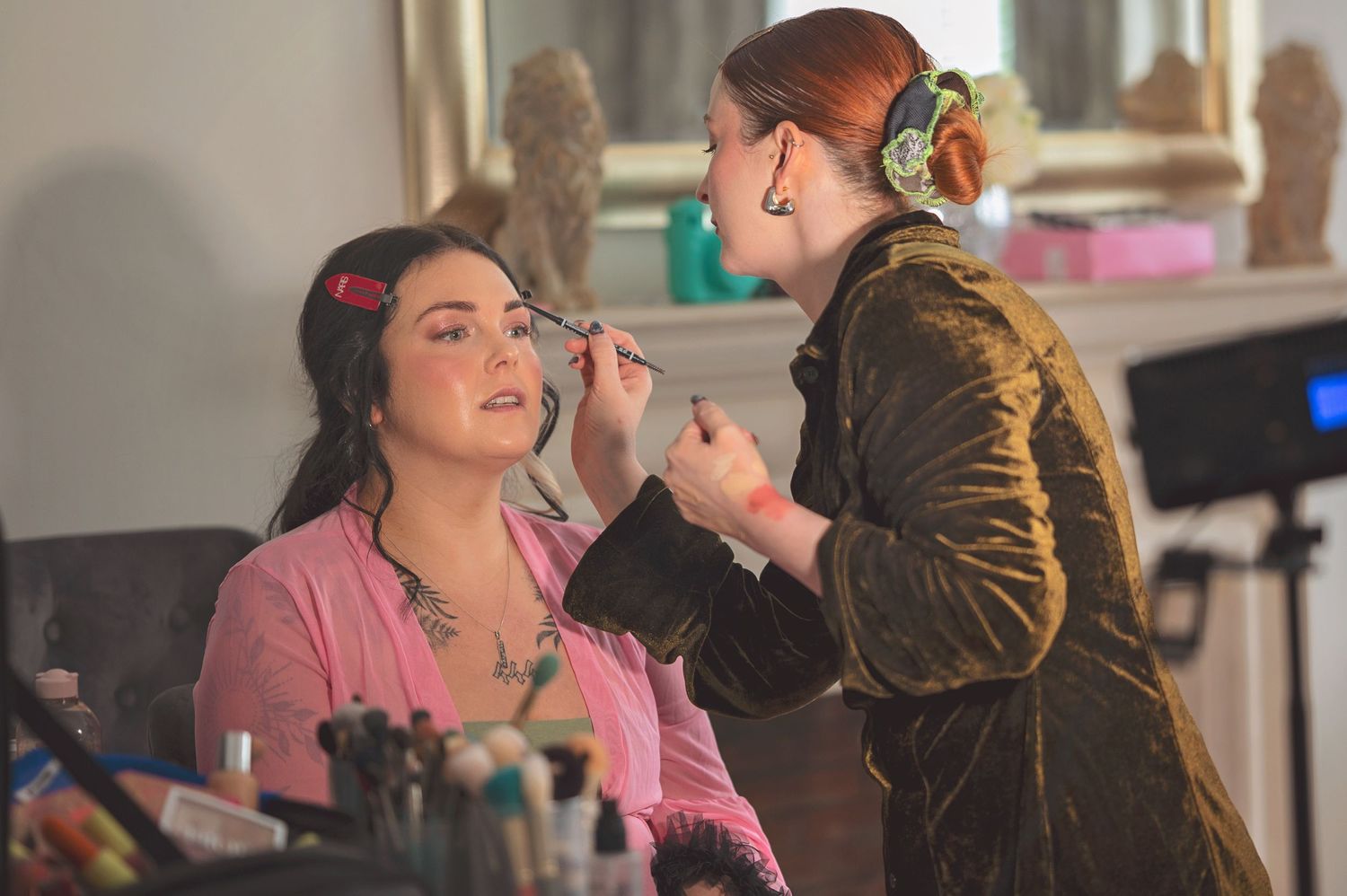 Professional makeup artist applying eye makeup to a bride in a pink top before her wedding.
