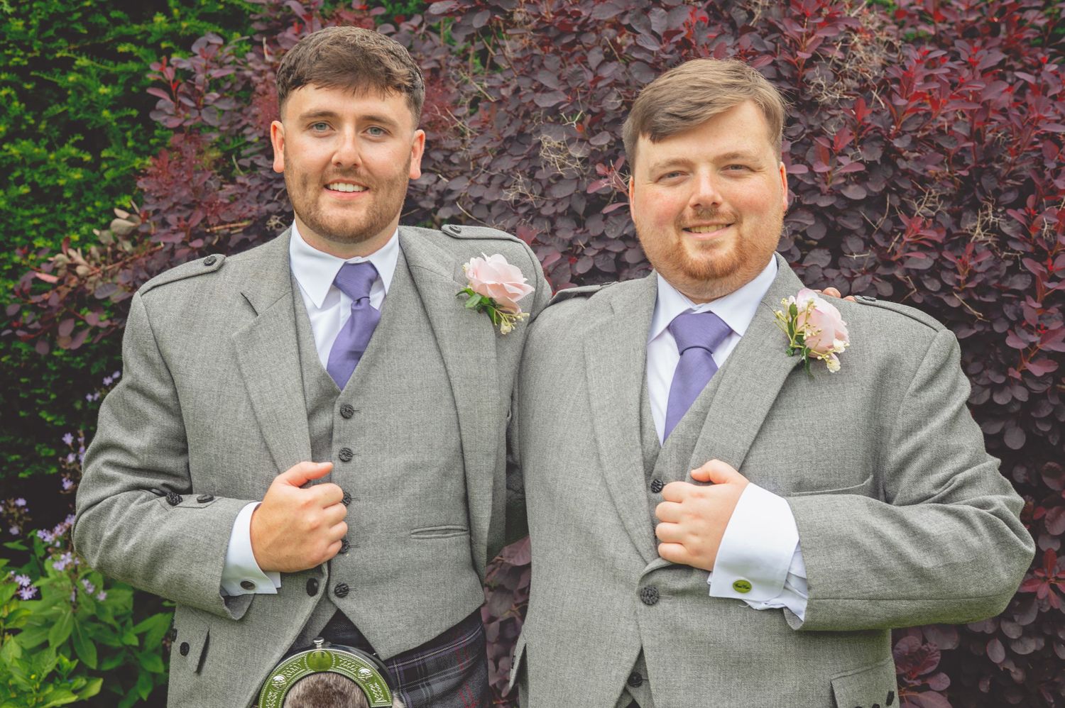 Groomsmen wearing matching grey suits and plaid accessories stand together outdoors.