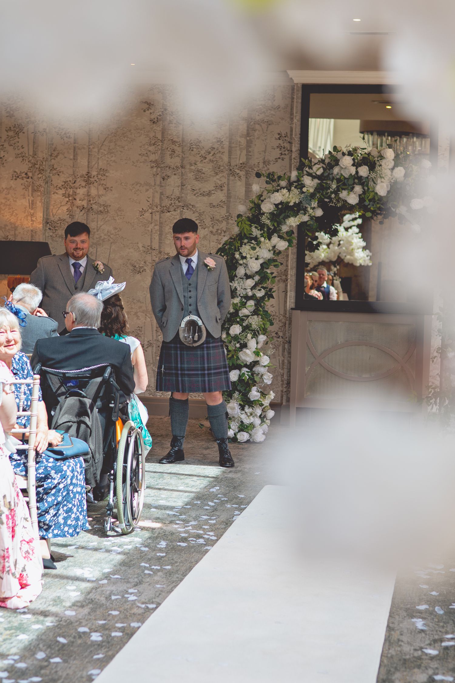 Wedding ceremony setup with white floral arch and guests seated in venue.