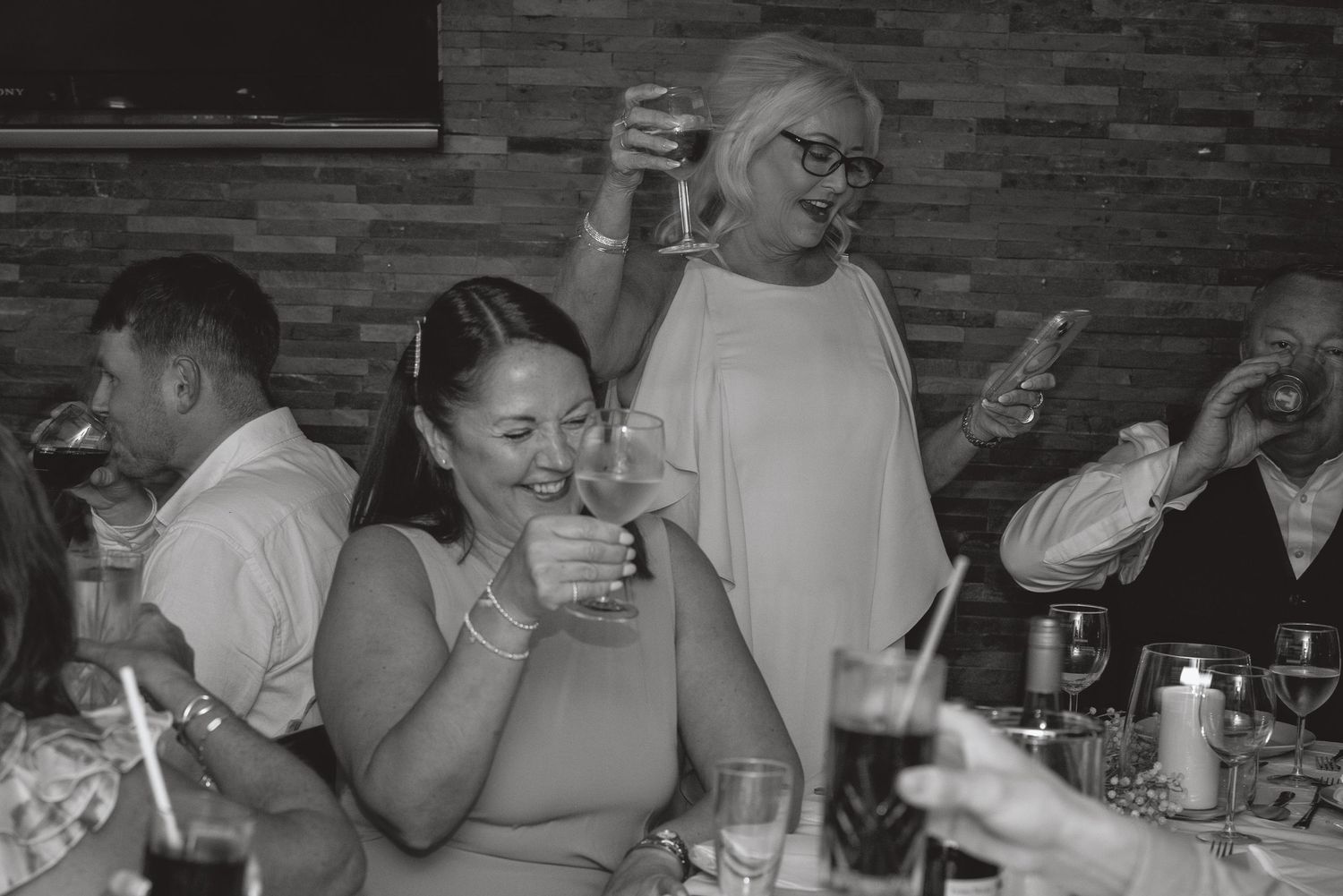 Wedding guests celebrate with drinks at a dimly lit reception venue.