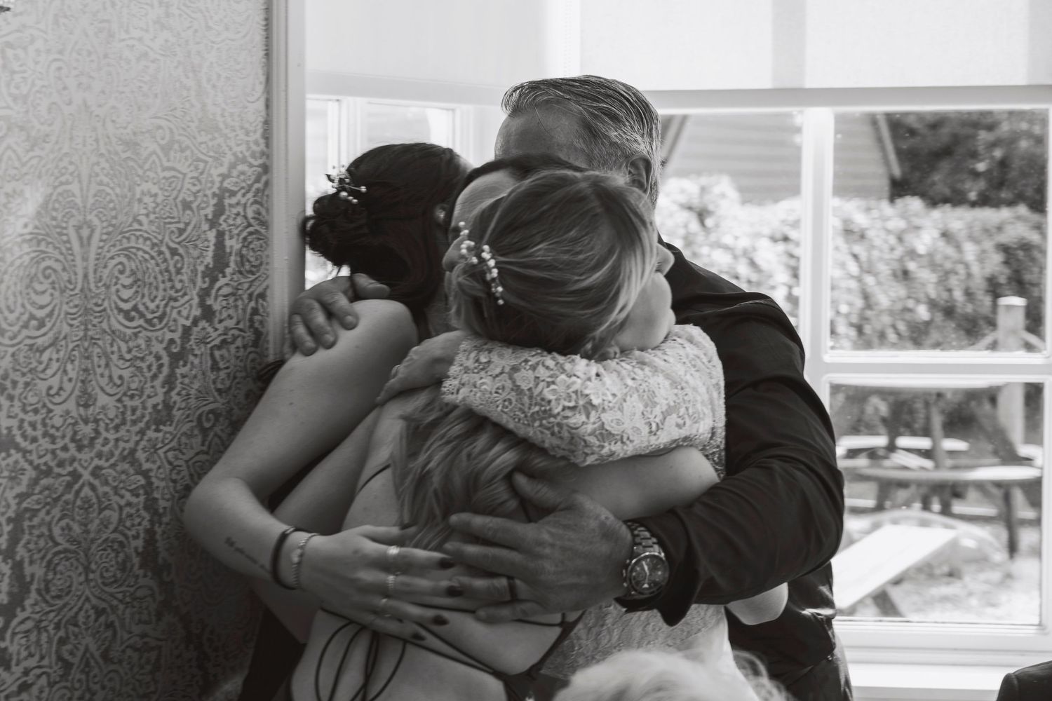 Black and white photo of three people sharing an emotional group hug at a wedding celebration.