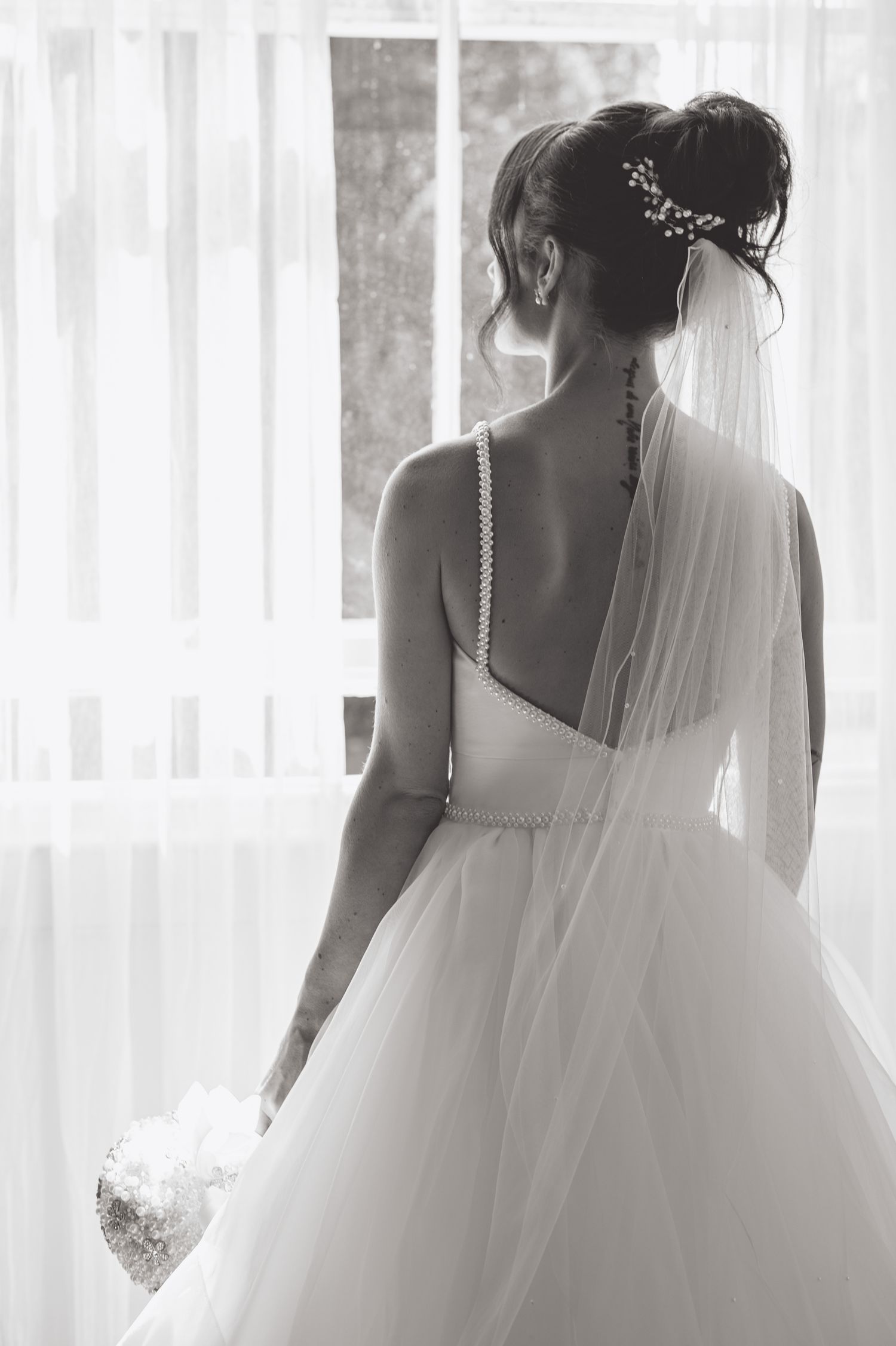Back view of a bride in white dress showing intricate details of her veil and pearl-adorned hairstyle.