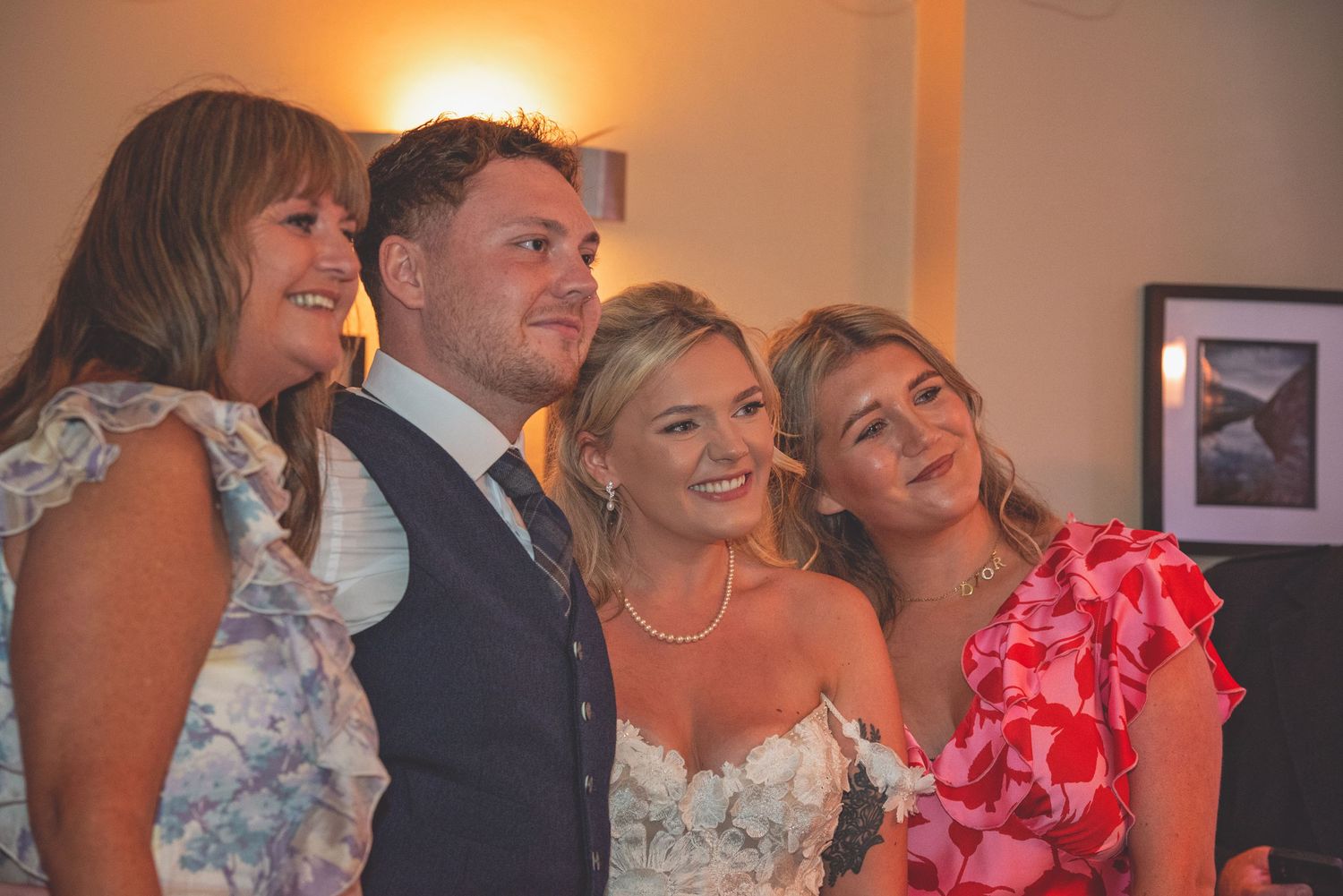 Wedding party group photo with guests in evening attire at reception.