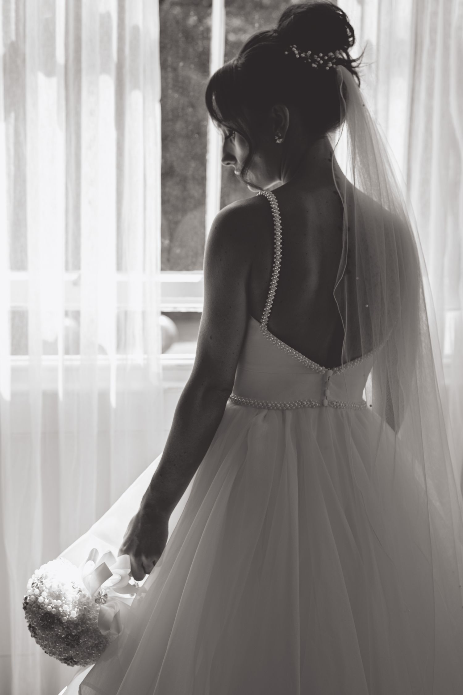 Silhouettes of a bride in a flowing wedding gown against white curtained windows.