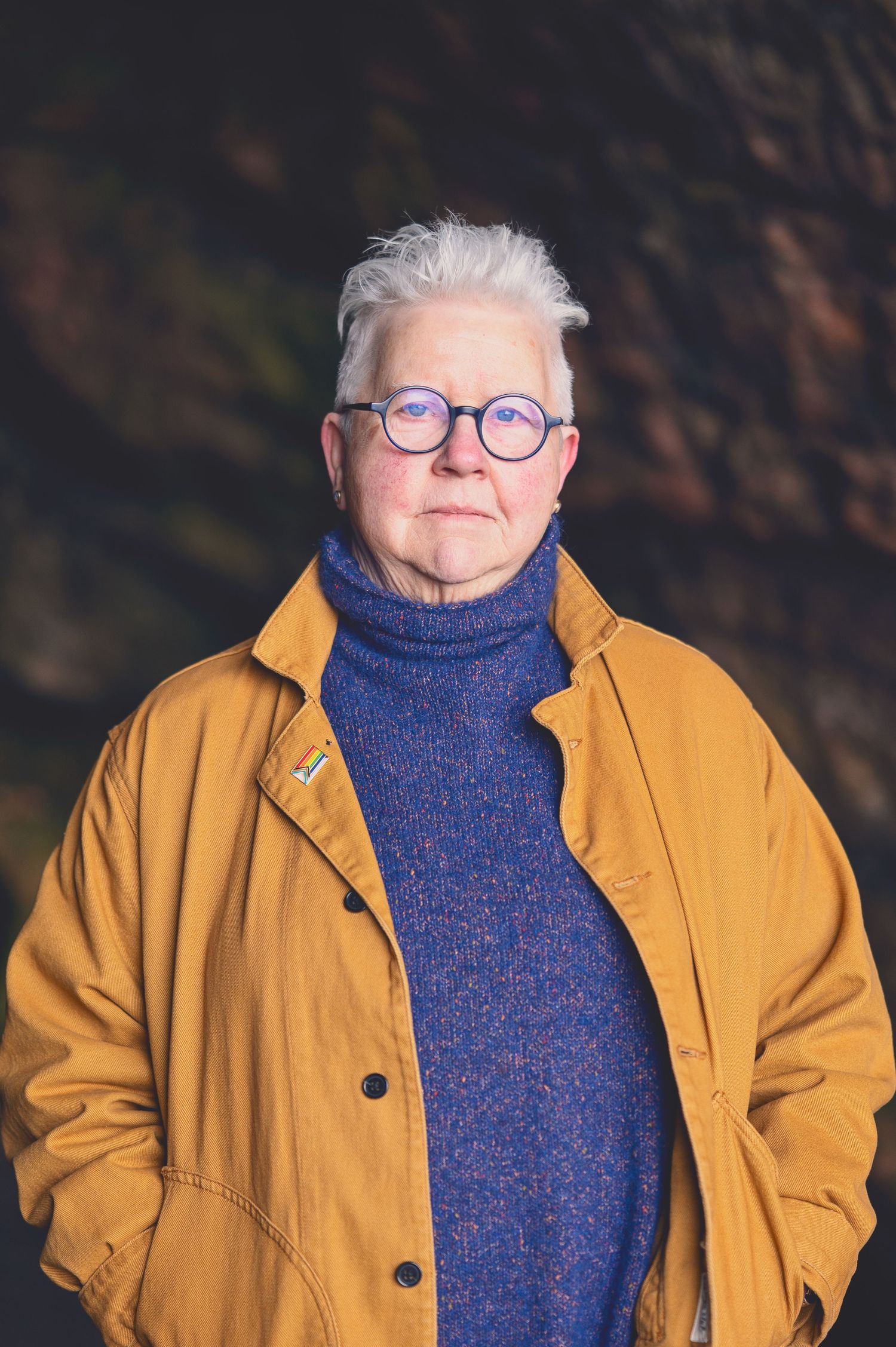 The Author Val Mcdermid with short white hair and round glasses wearing a mustard jacket and blue turtleneck sweater in the Weymss caves