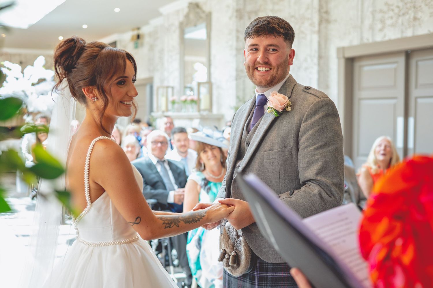 A couple exchanges rings during their wedding ceremony surrounded by white floral decorations.