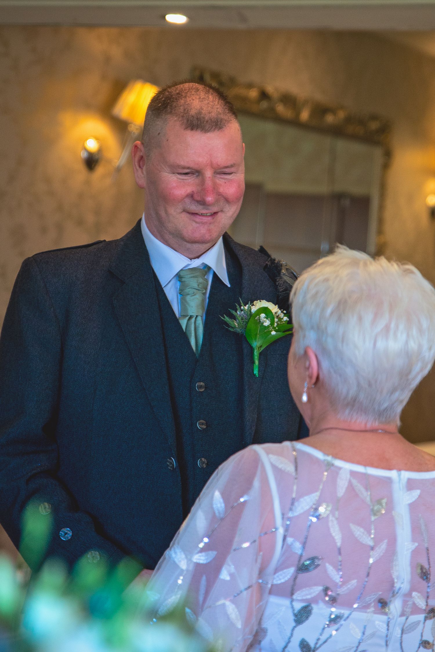 Groom in dark suit smiling during wedding reception conversation.