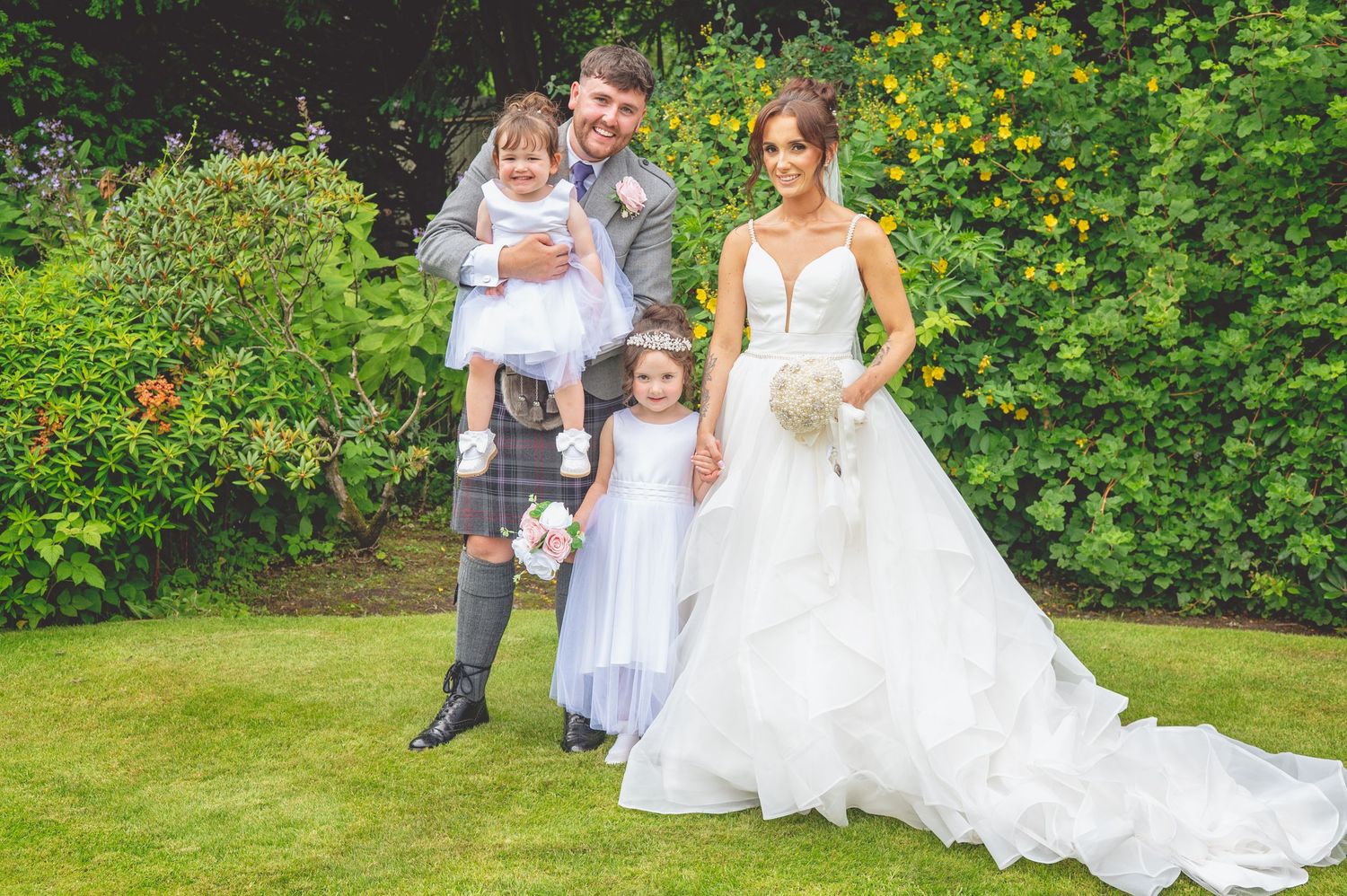 Wedding party poses on garden lawn with children in formal attire.