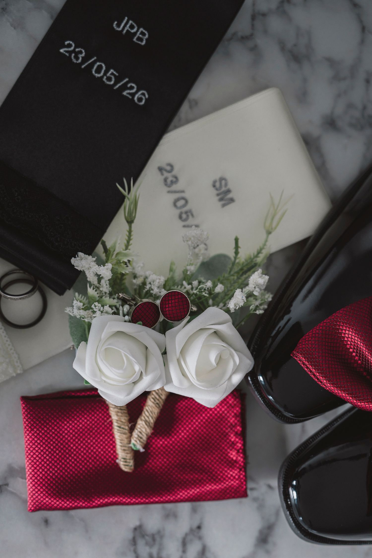 Wedding boutonniere with white roses on red pocket square beside monogrammed keepsake boxes dated 23/05/26.