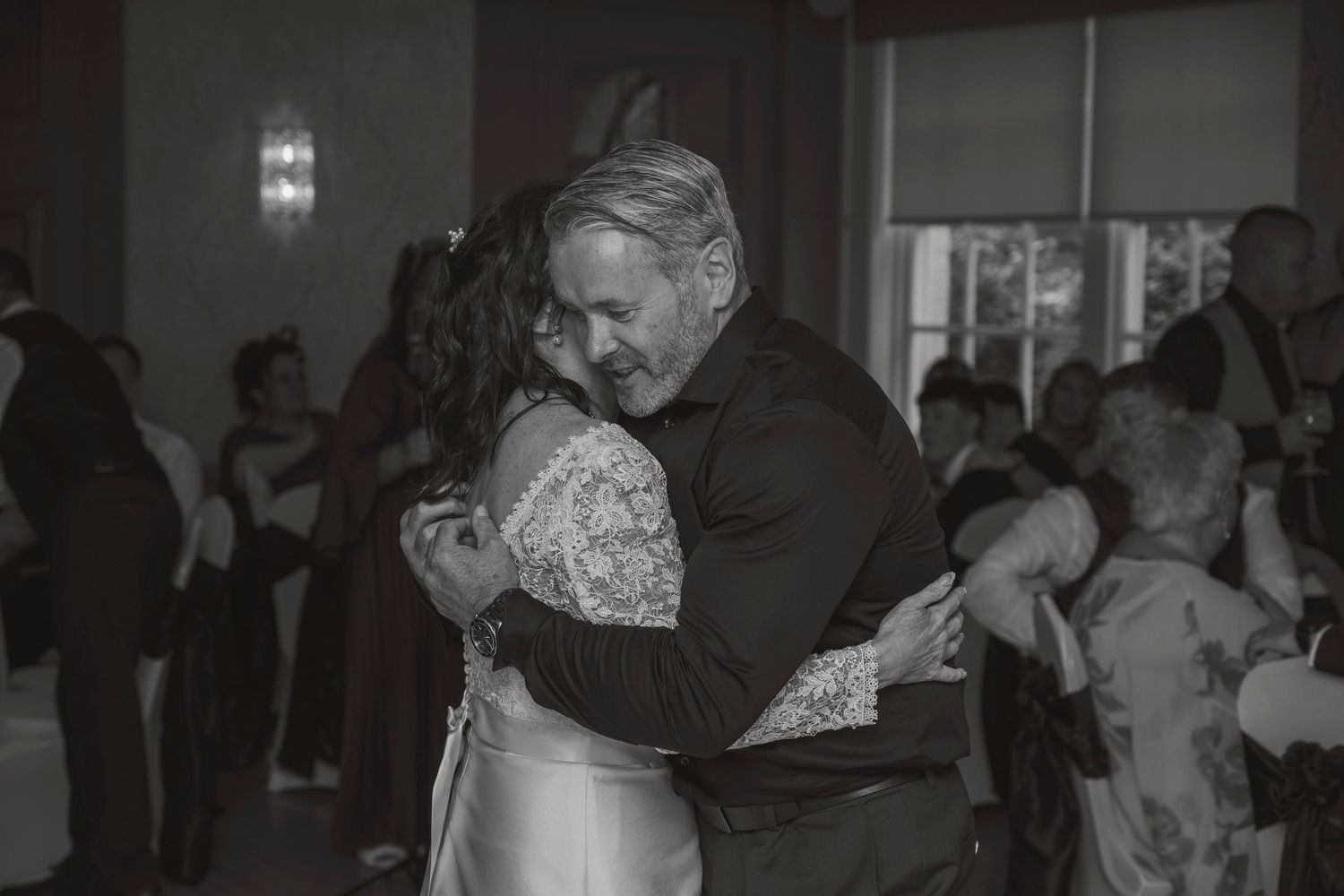 Black and white photo of a couple sharing an emotional dance embrace at a wedding reception.