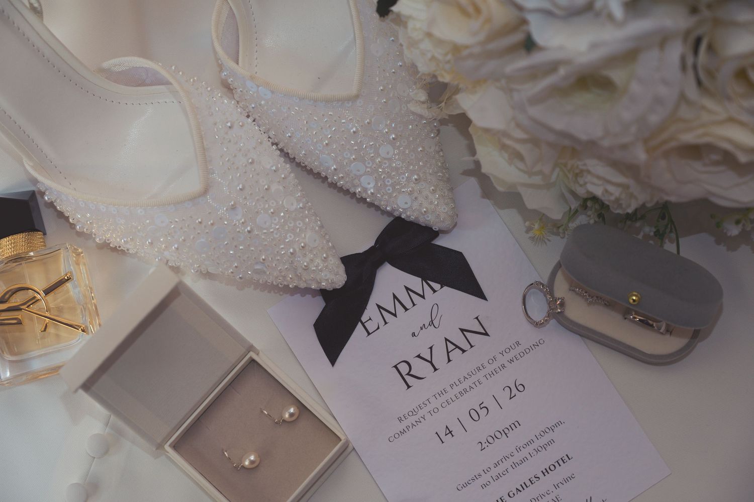 Elegant wedding flat lay with pearl shoes, floral bouquet, invitation for Emma & Ryan, earrings, and gold accessories.