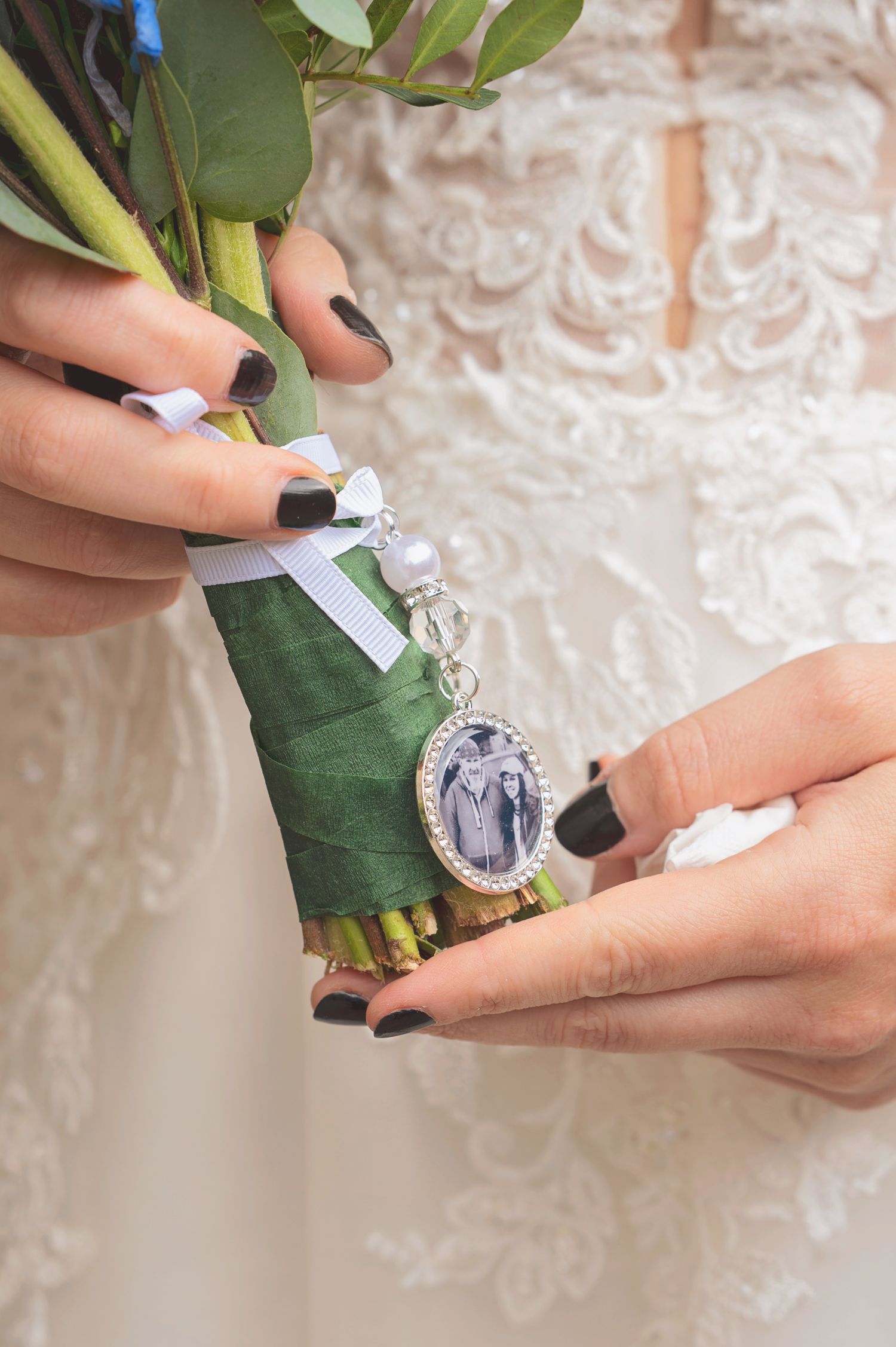 Bride holding wedding bouquet with silver oval photo charm pendant and pearl ribbon memorial keepsake.