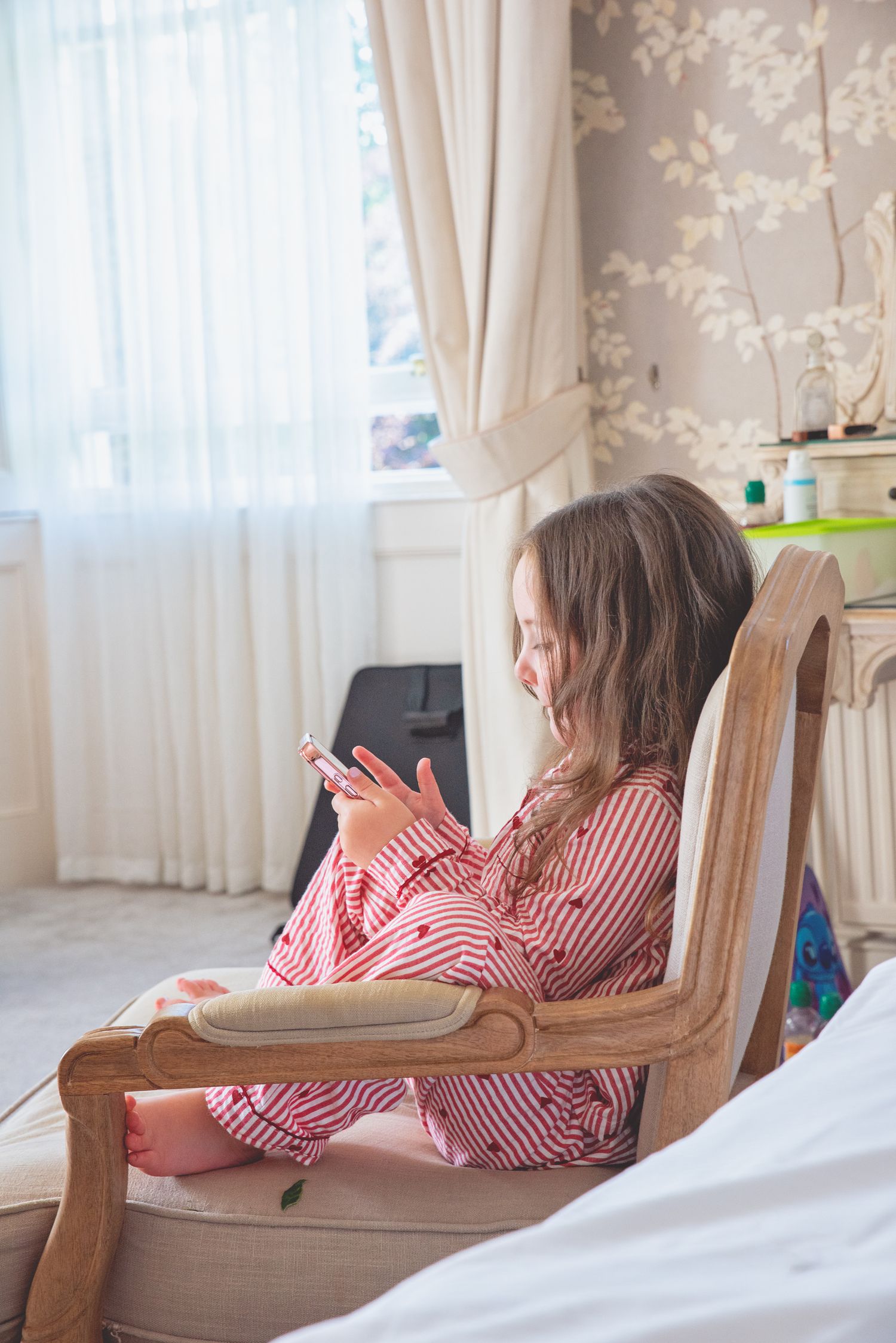 Person in striped pajamas relaxing in vintage chair while checking phone.