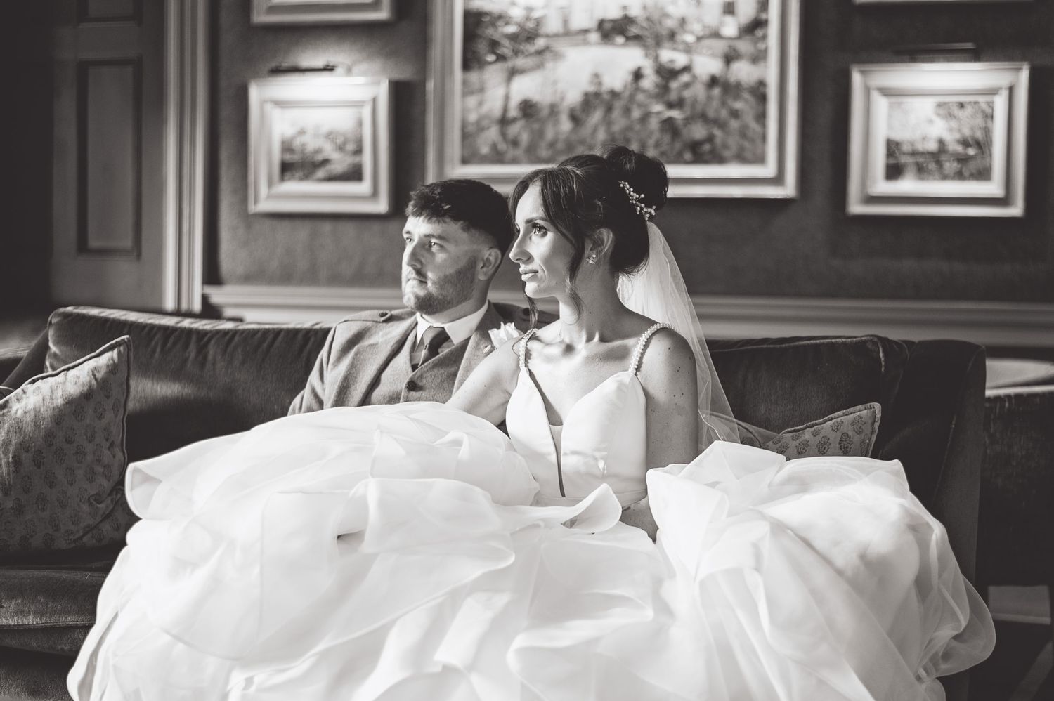 Bride in white gown relaxes on vintage couch in elegant indoor setting.