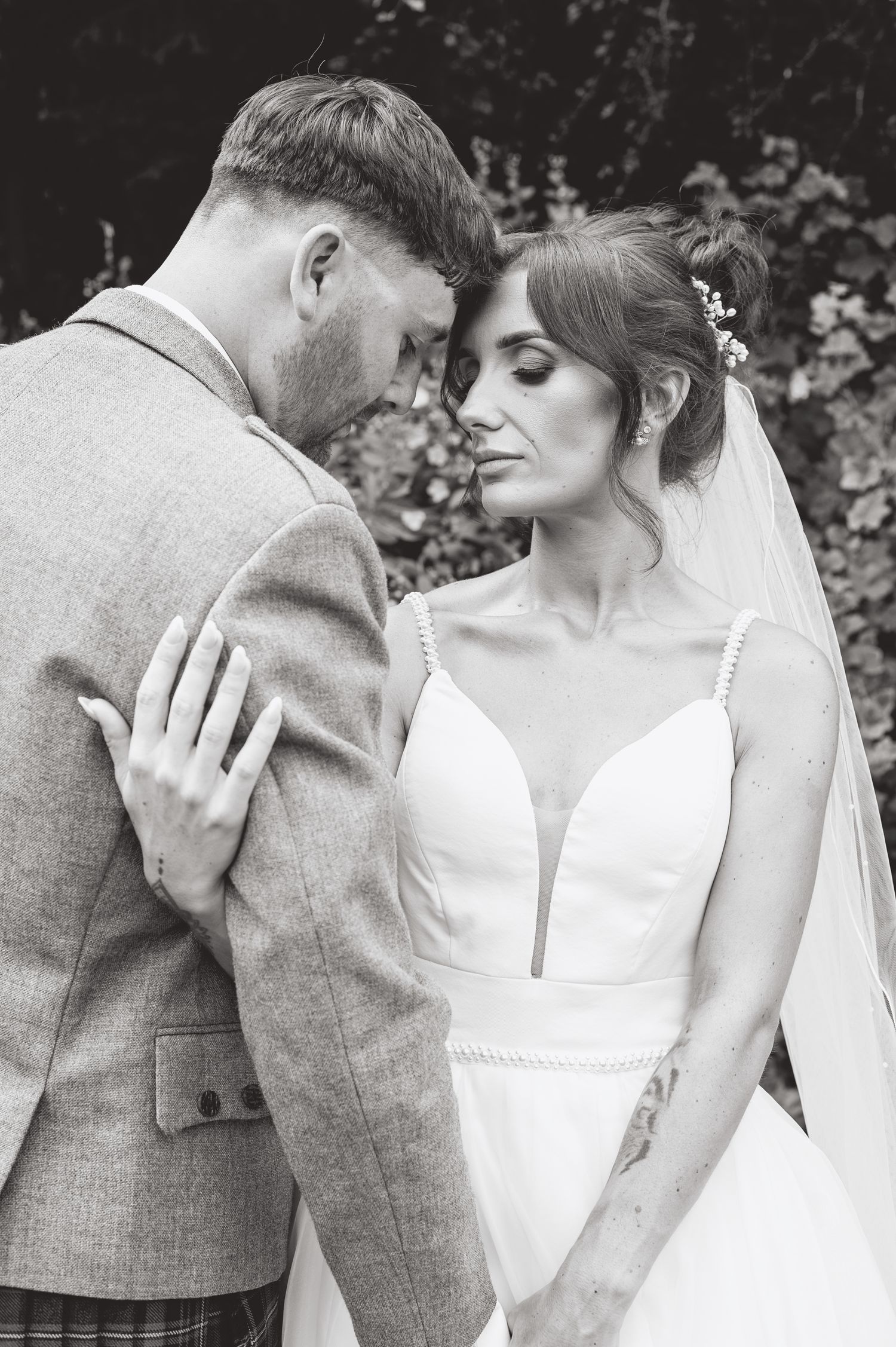 Black and white wedding portrait of a couple sharing an intimate moment in a garden setting.