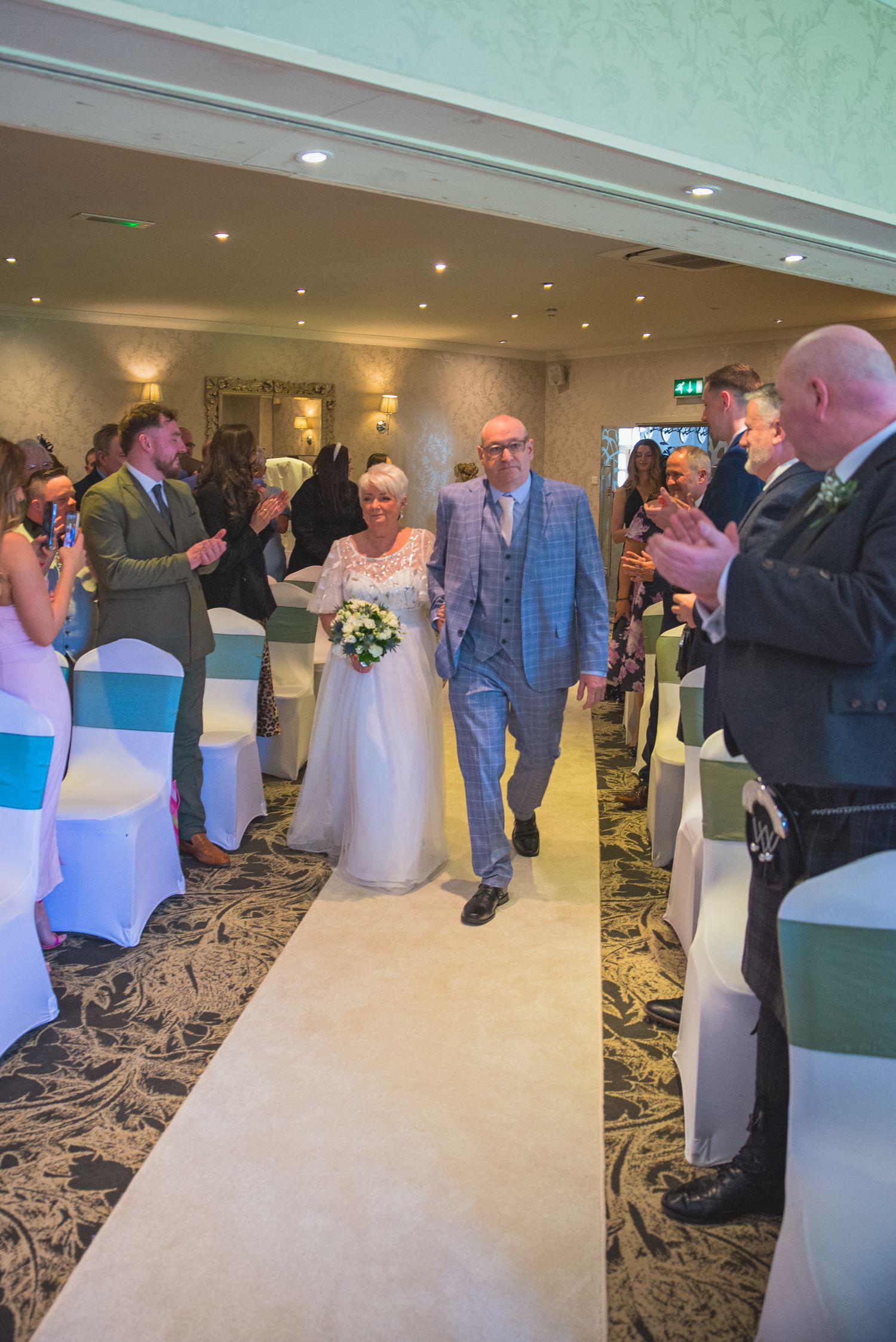 Wedding celebration in an elegant banquet hall with white chair covers and decorative lighting.