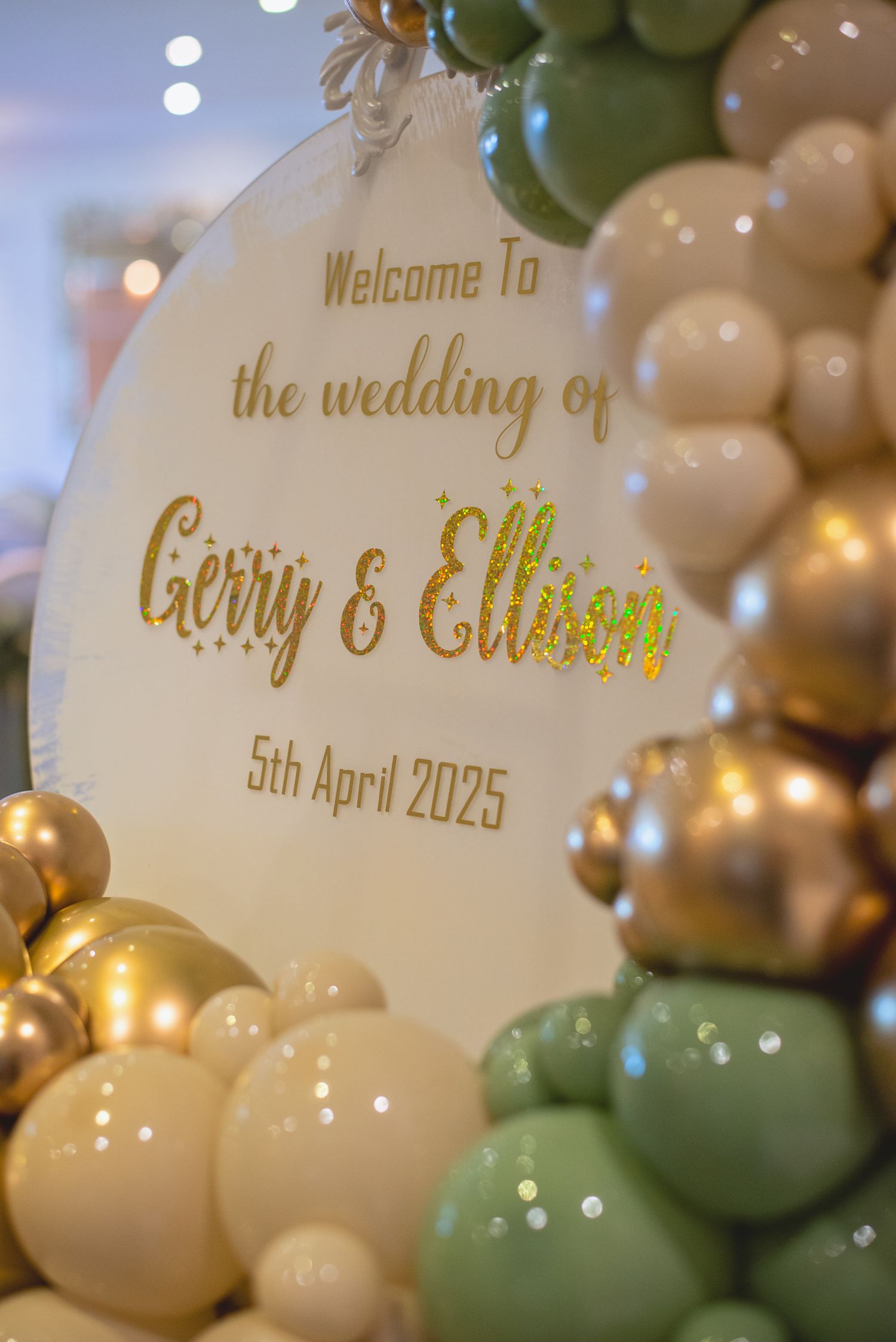 Gold lettering on a wedding welcome sign surrounded by pastel balloon decorations.