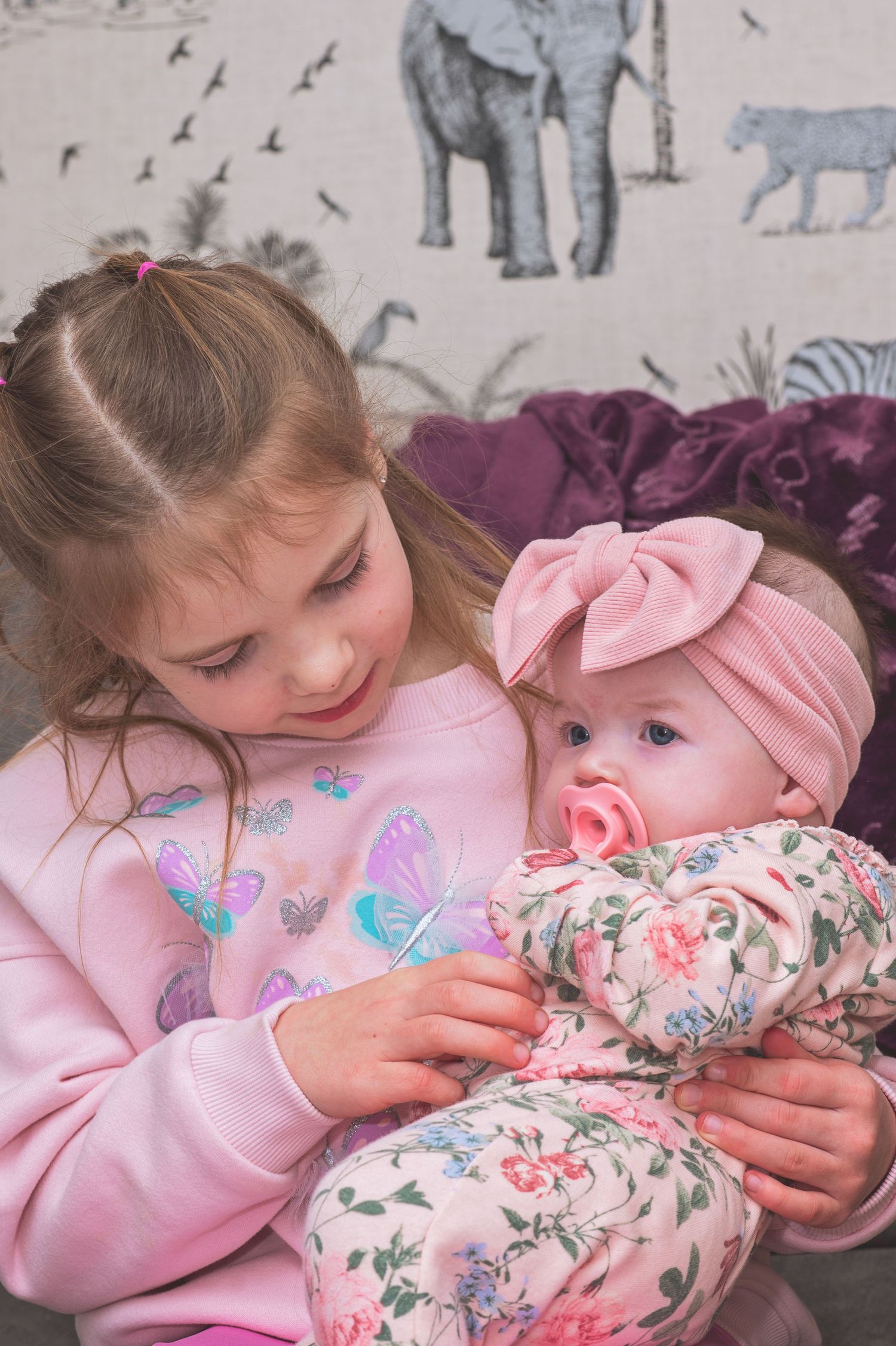 A tender moment between siblings as an older child in pink gently embraces a baby in floral print clothing.