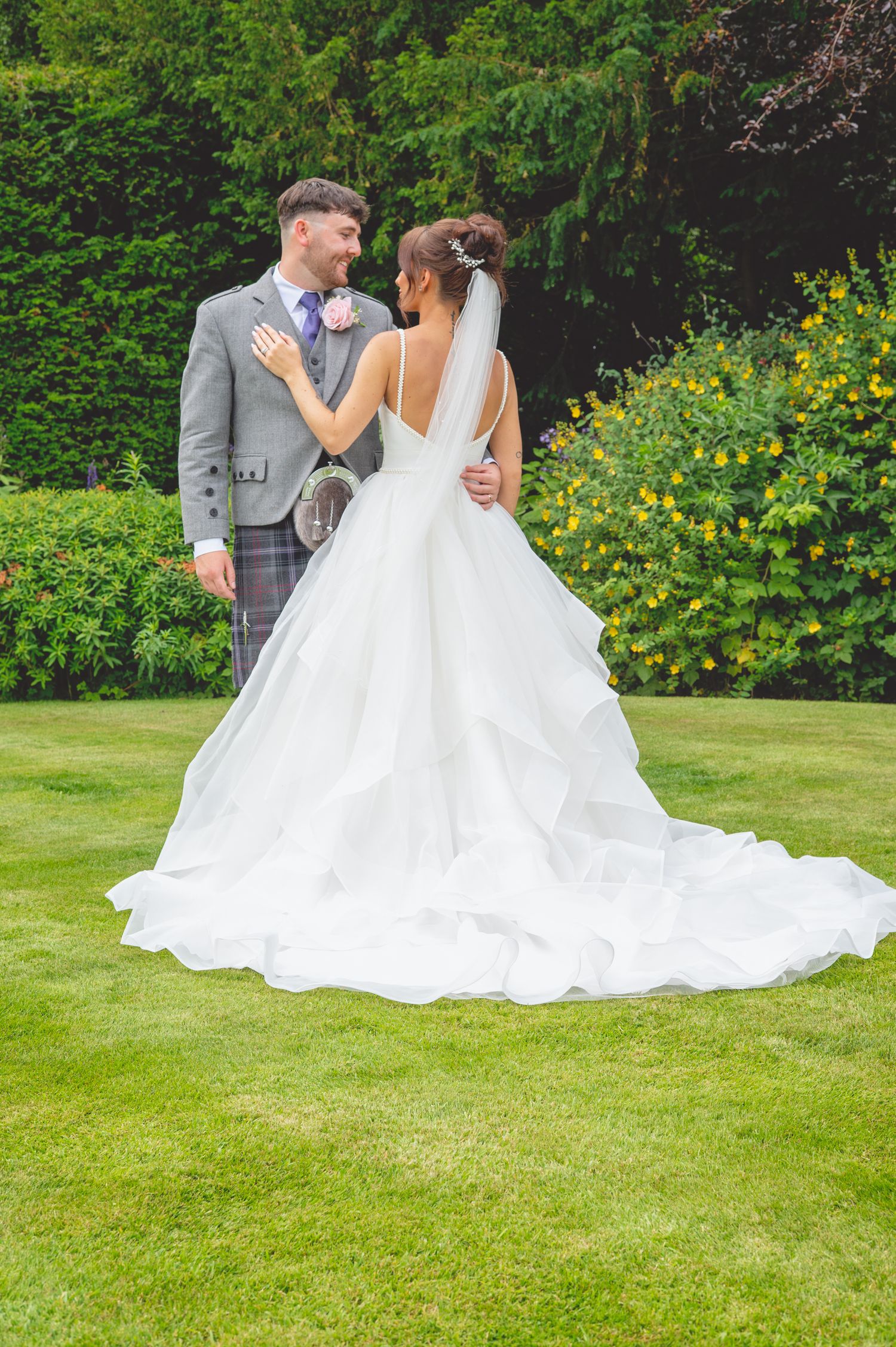 Wedding couple poses on manicured lawn with bride's dramatic train in full display.