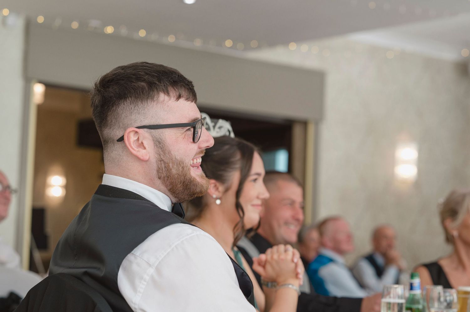 Guests laughing and smiling during wedding reception speeches in an elegant venue.