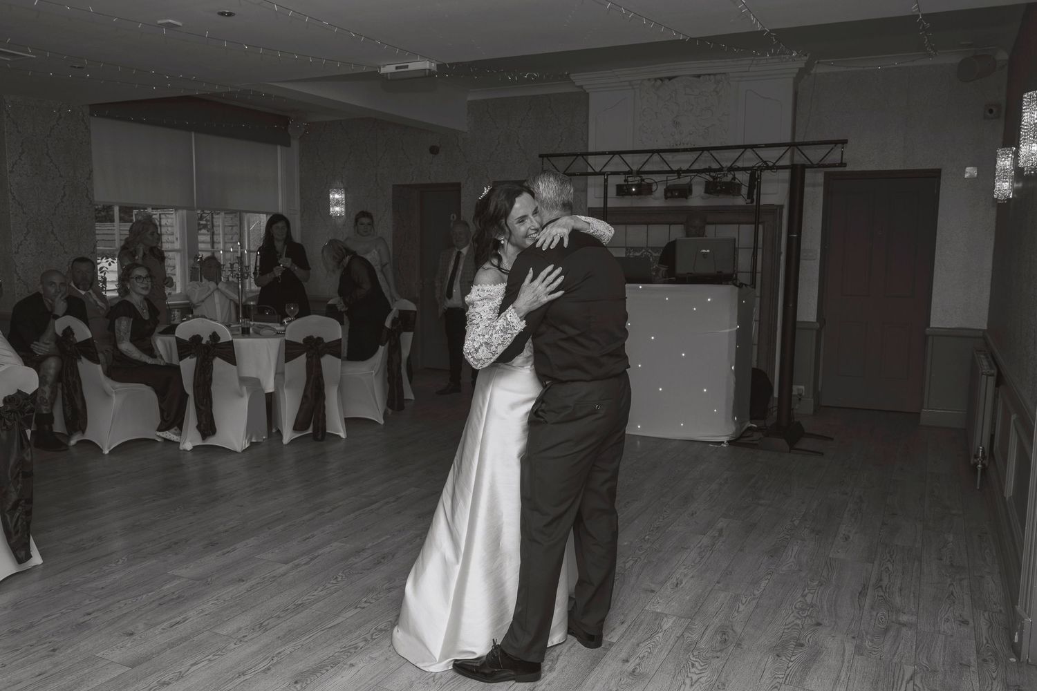 Black and white photo of a bride and groom sharing their first dance at a wedding reception venue.