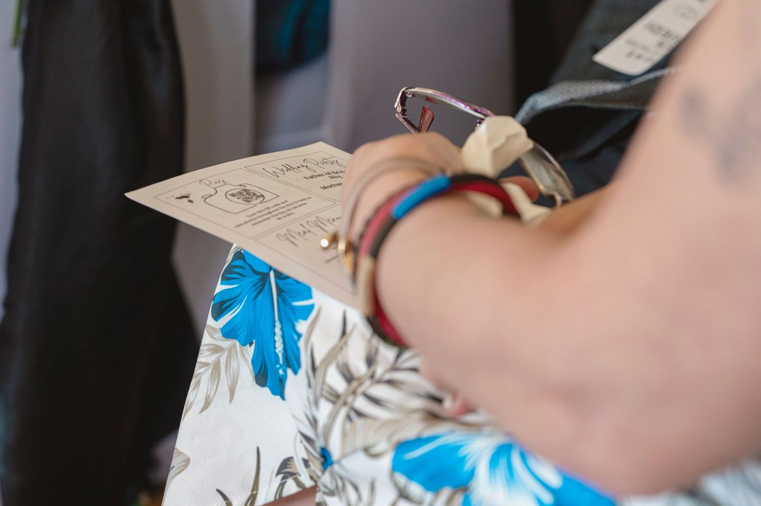Close-up of a person wearing colorful bracelets and a floral shirt, holding a vintage-style card or ticket.