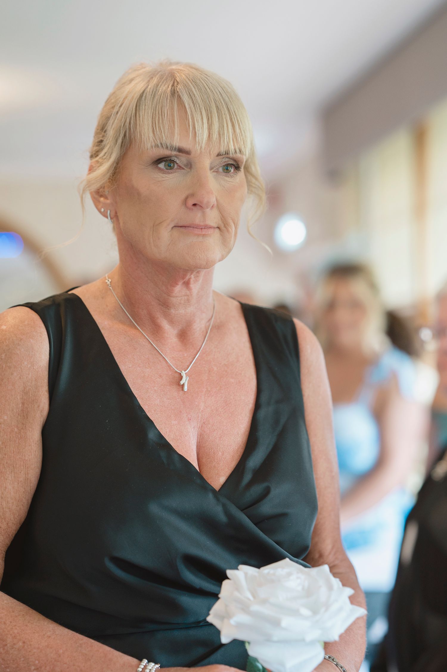 Elegant older woman in a dark green satin dress holding a white rose at a formal event.