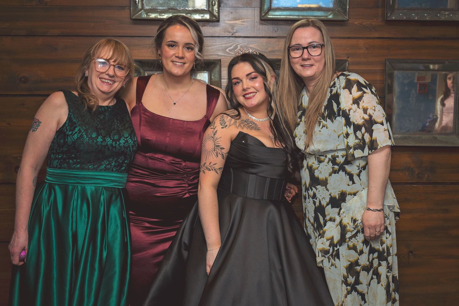 Four women posing together in formal evening gowns at a wedding reception celebration.