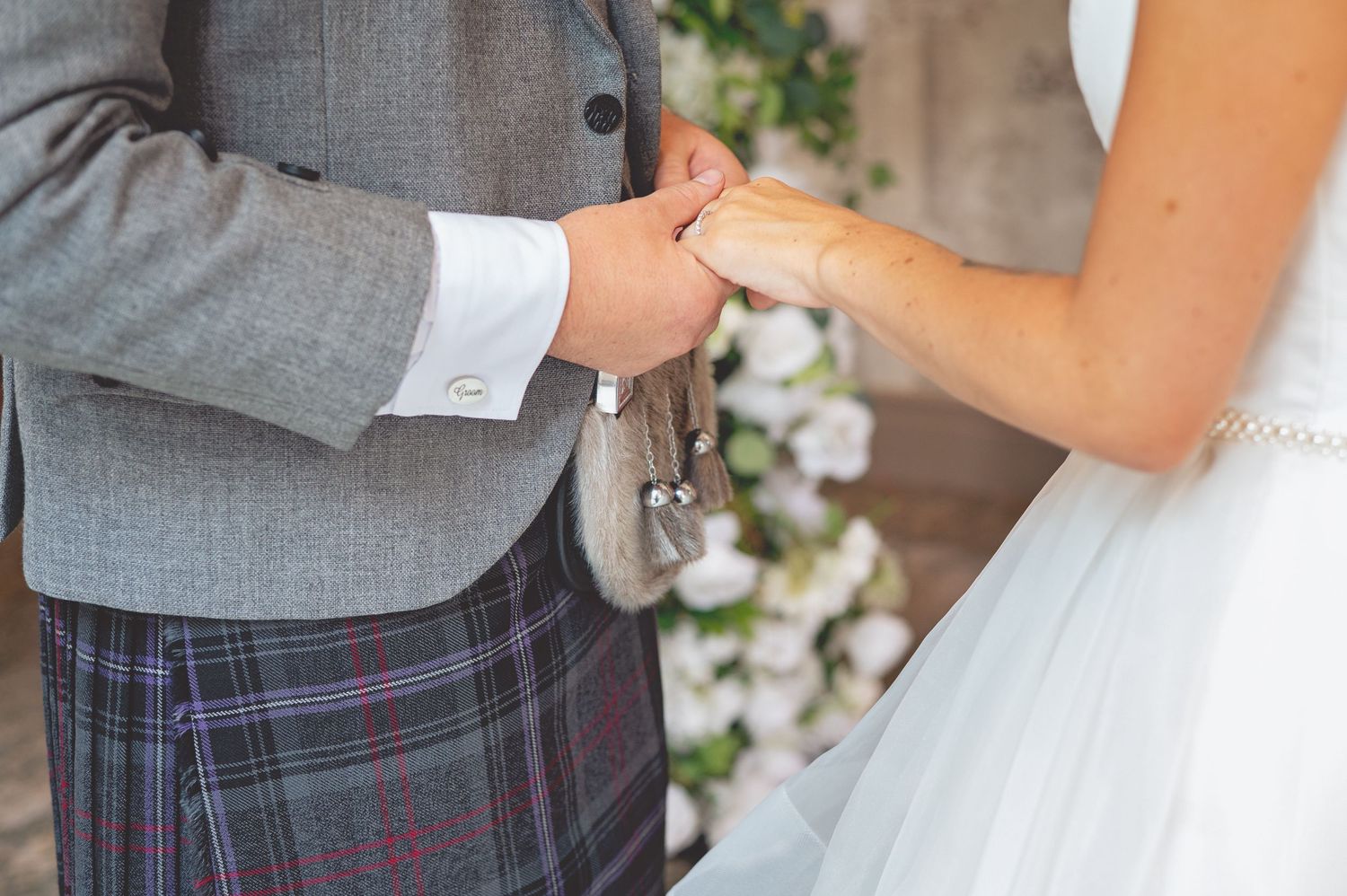 Wedding couple holding hands with groom wearing traditional Scottish kilt and grey jacket.