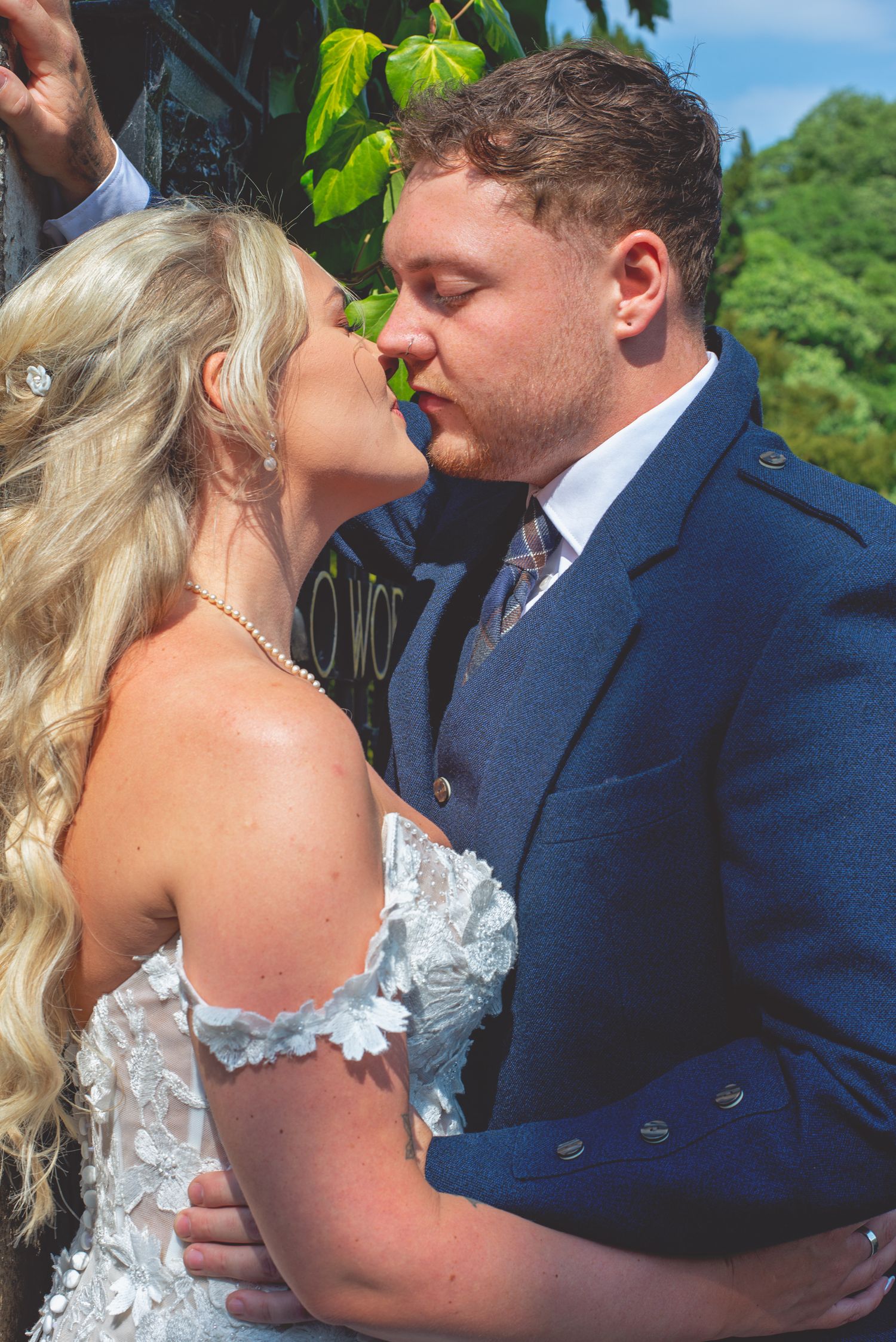 Intimate wedding couple moment captured in color against green foliage background.