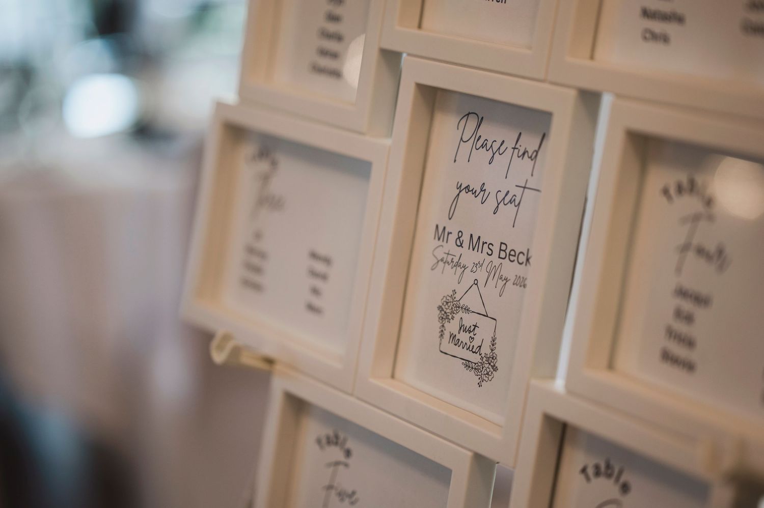 Elegant white framed wedding seating chart cards displayed on a wall for Mr & Mrs Beck's reception.