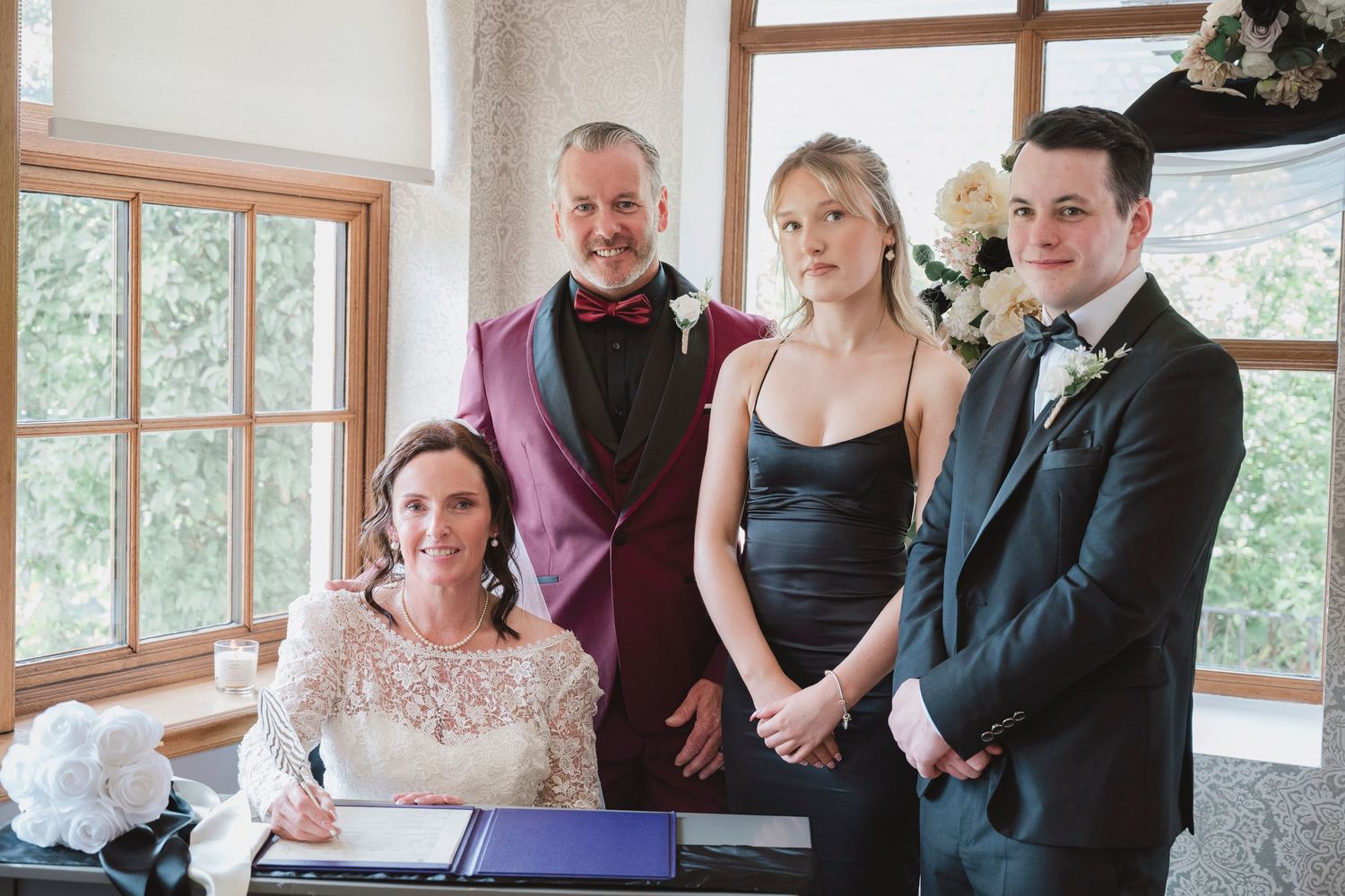 Bride signs wedding register surrounded by groom and witnesses at elegant indoor ceremony.