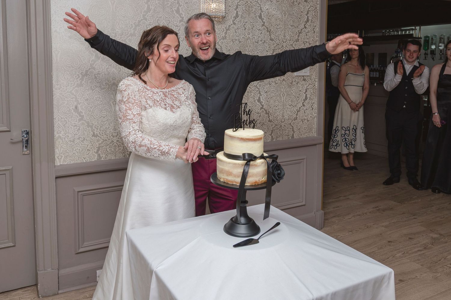 Bride and groom joyfully cutting their wedding cake together at their reception venue.