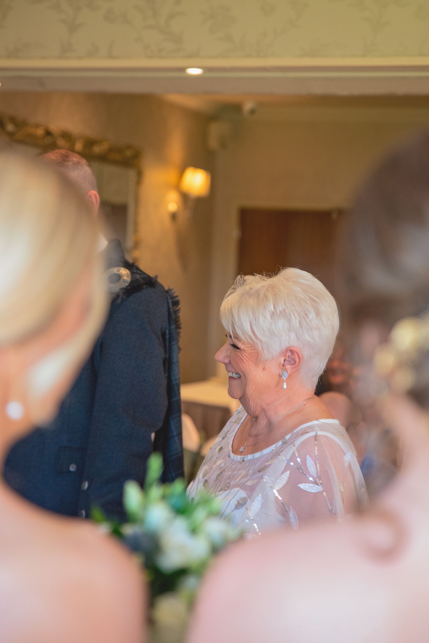 Wedding guest in lace dress smiling during indoor reception celebration.