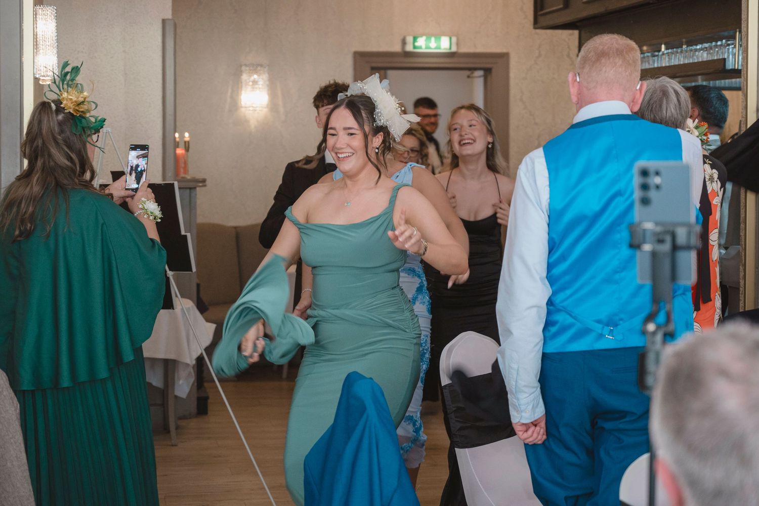 Woman in teal gown dancing joyfully at an elegant indoor wedding reception celebration.