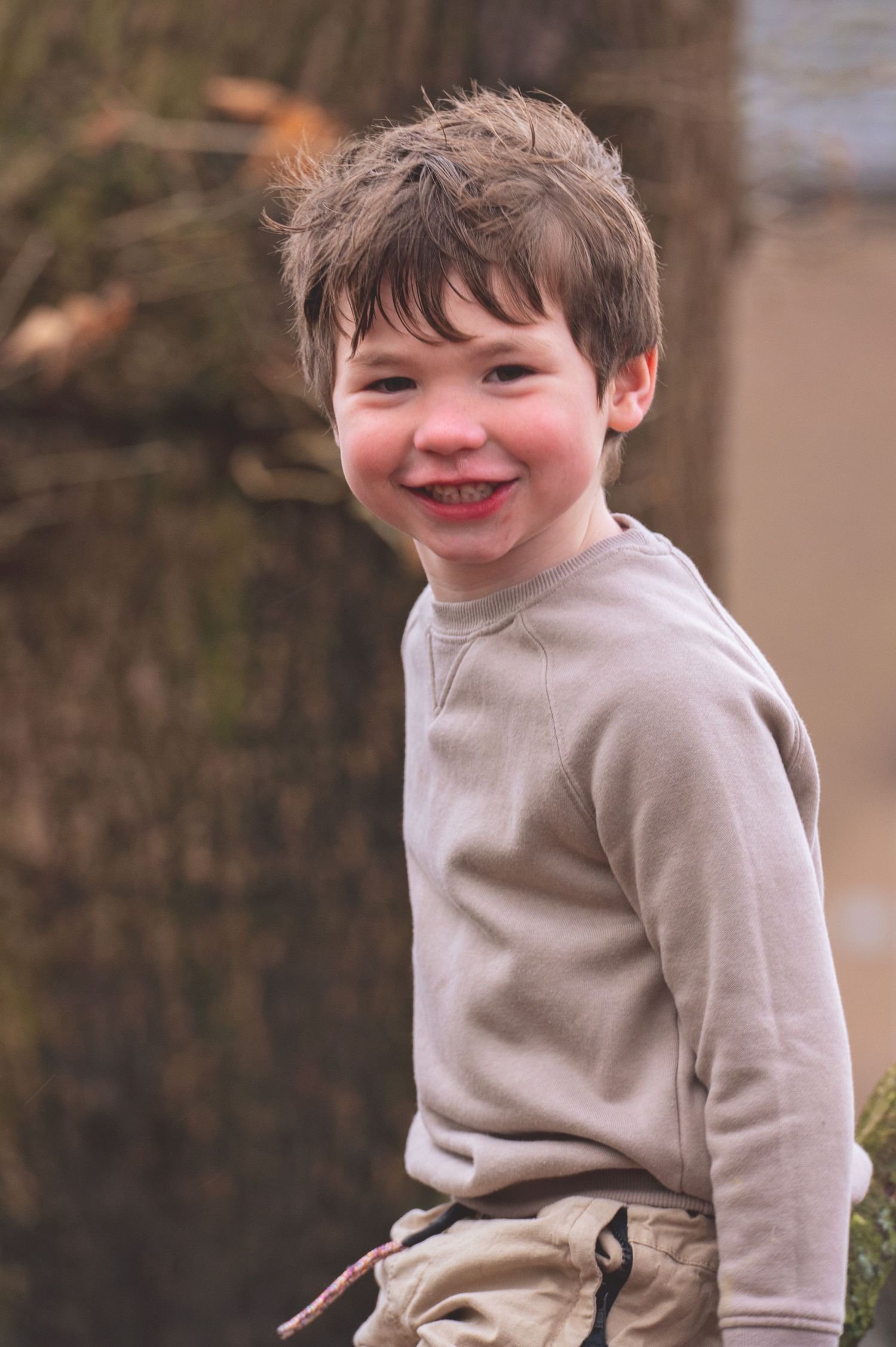 A young child in a beige sweater smiles and laughs while playing outdoors.