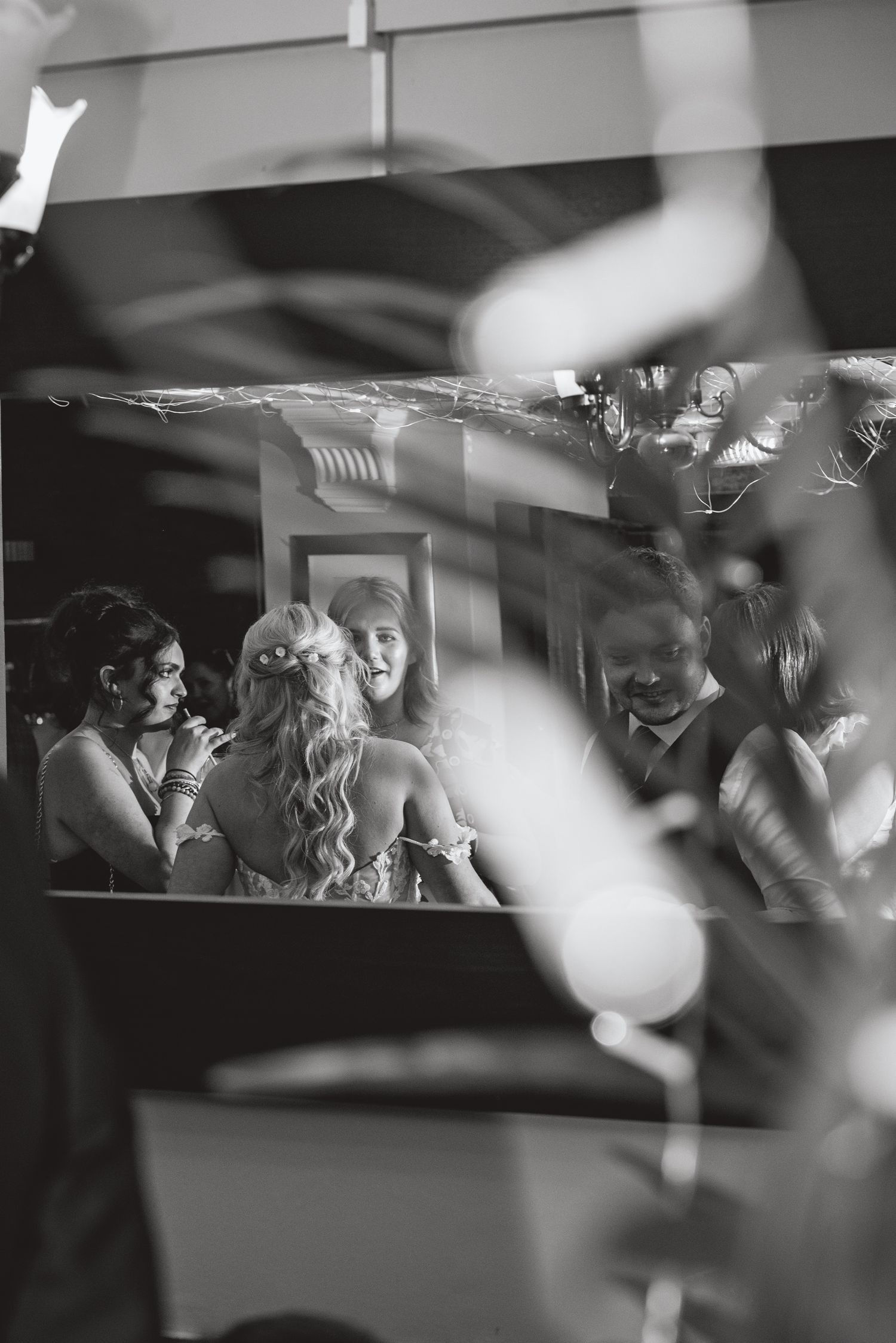 Artistic black and white photo of wedding guests through blurred foreground elements.