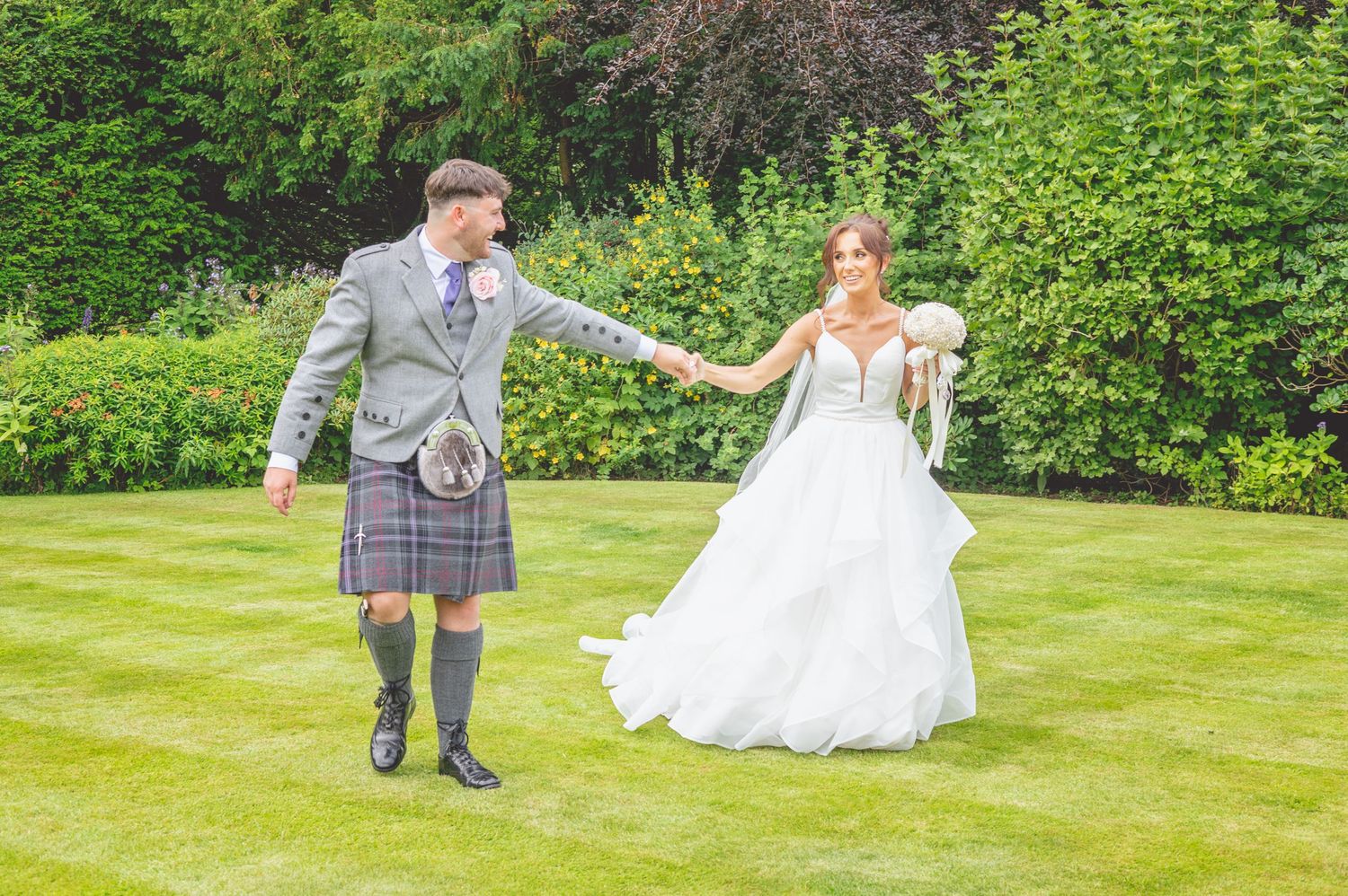Wedding couple shares playful moments on a sunlit garden lawn.
